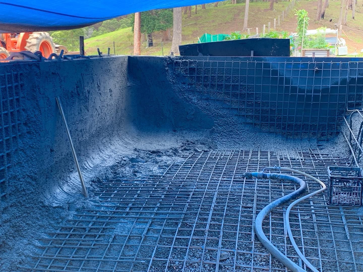 Pool construction: Concrete being applied to the interior, metal rebar grid visible, blue tarp overhead. — HinterCoast Pools In Cooroy, QLD