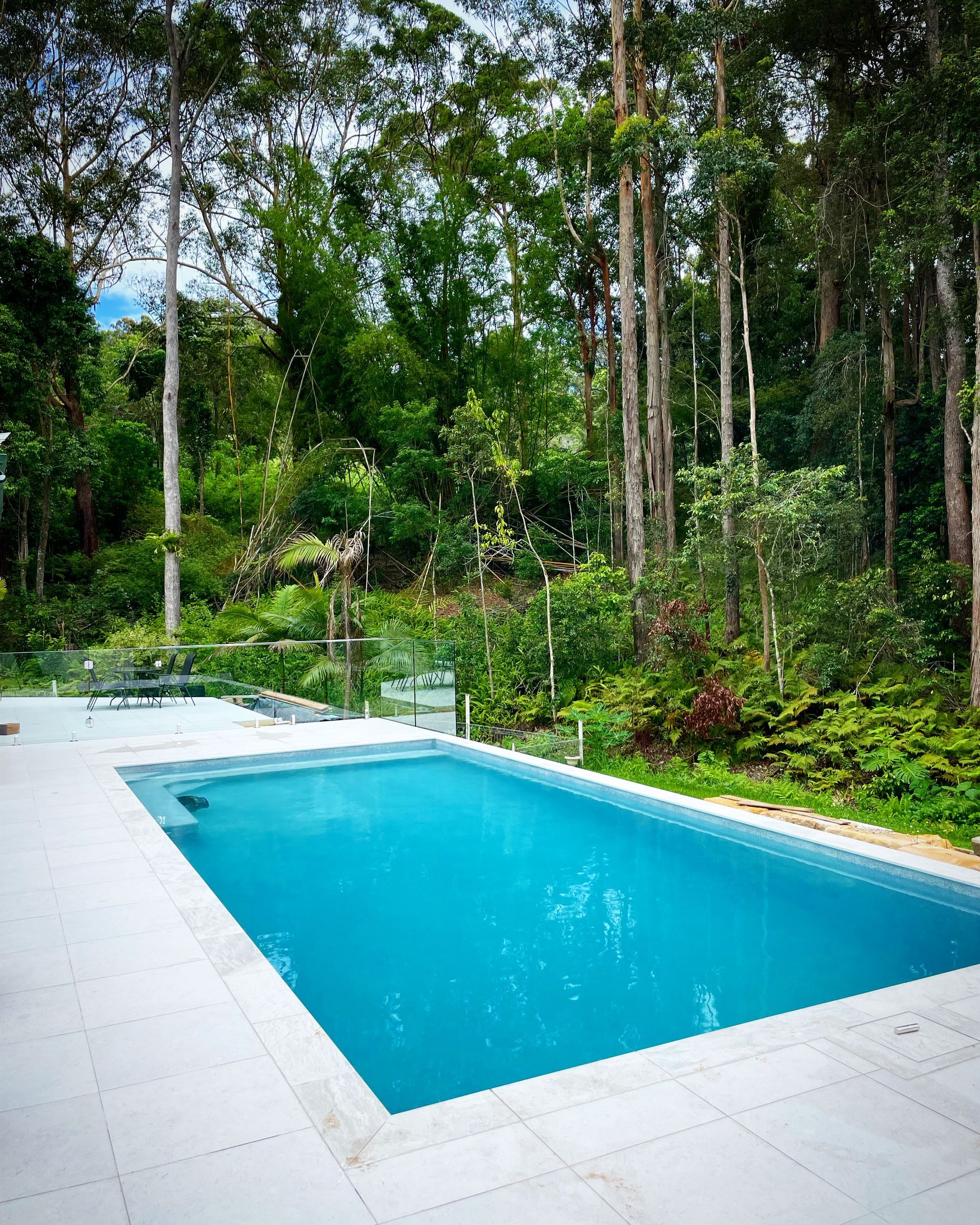 Rectangular pool with turquoise water surrounded by light gray tiles, set against a lush green forest backdrop. — HinterCoast Pools In Wolvi, QLD