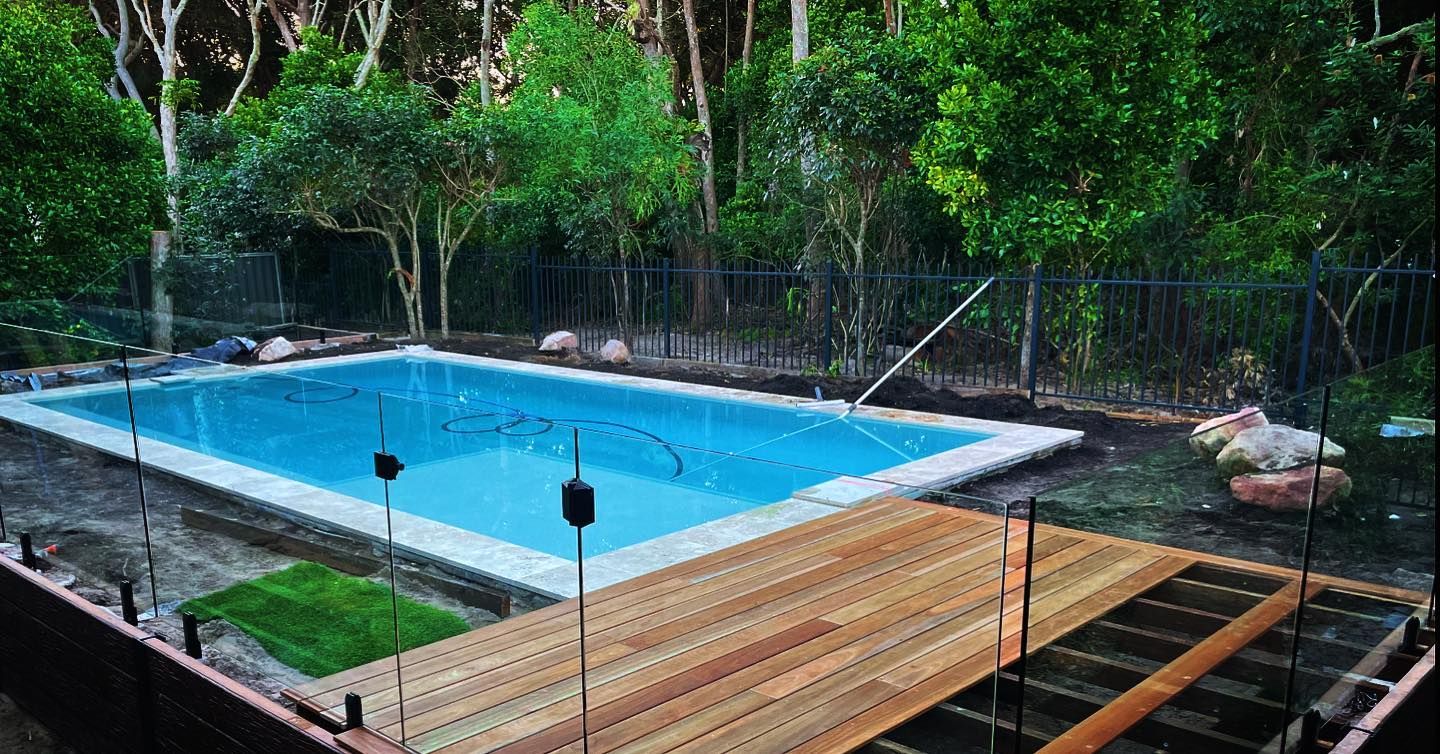 Rectangular pool with wooden deck, surrounded by trees and a black fence. — HinterCoast Pools In Wolvi, QLD