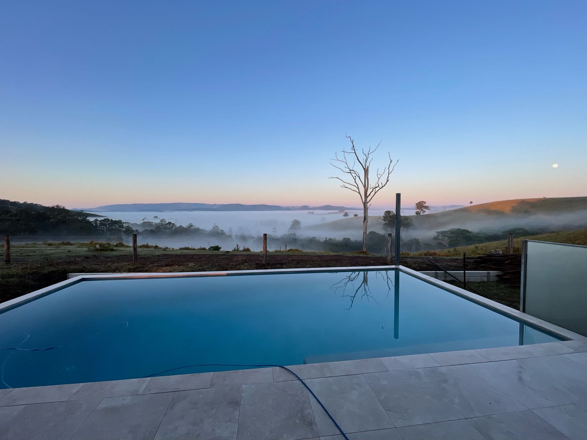 Infinity pool overlooking a misty valley at dawn. Blue sky, water, and landscape. — HinterCoast Pools In Wolvi, QLD