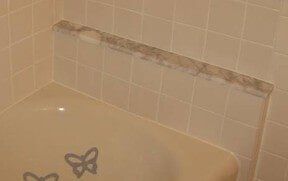Tan bathtub with a tiled wall and shelf.