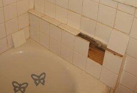 Damaged bathroom tile revealing wood.