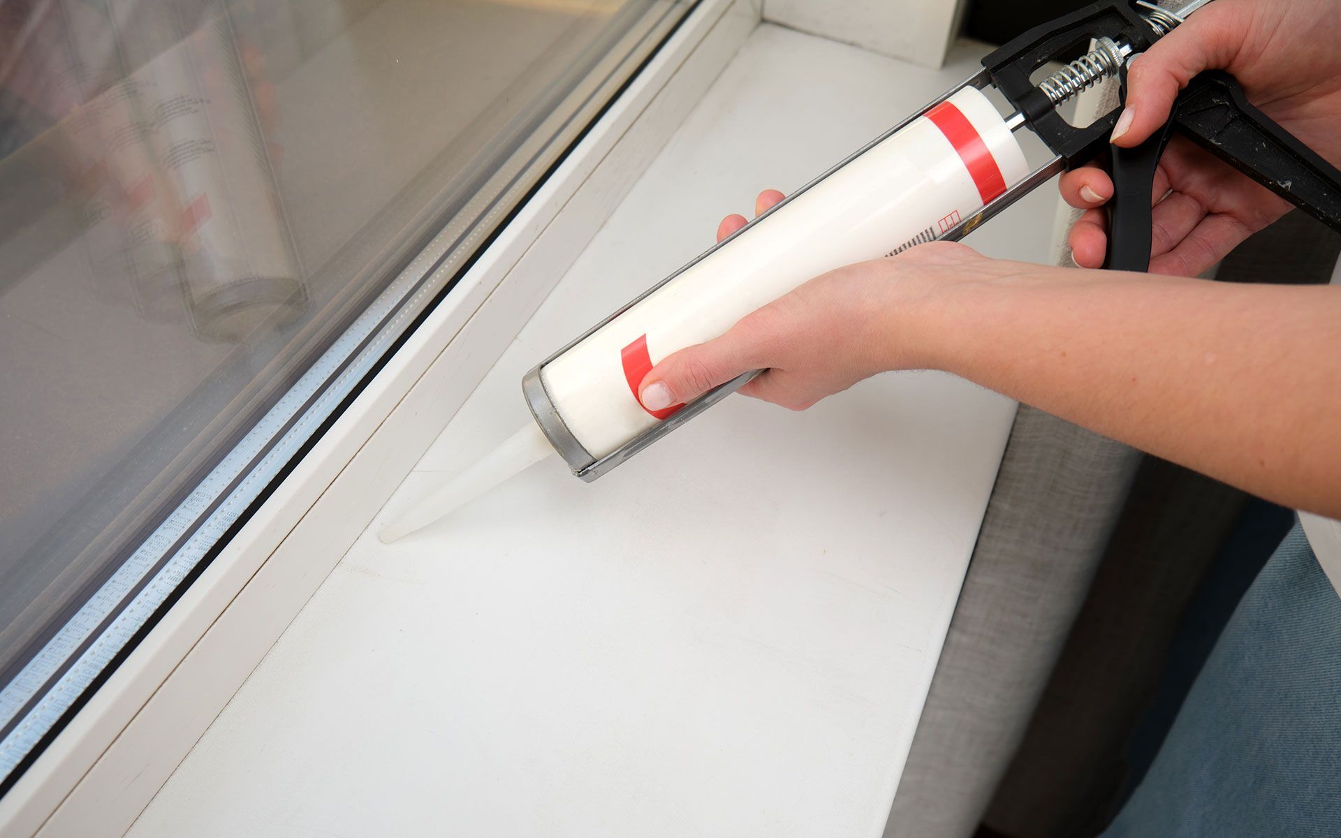 Person sealing a window frame with a caulk gun. White caulk being applied to the seam.