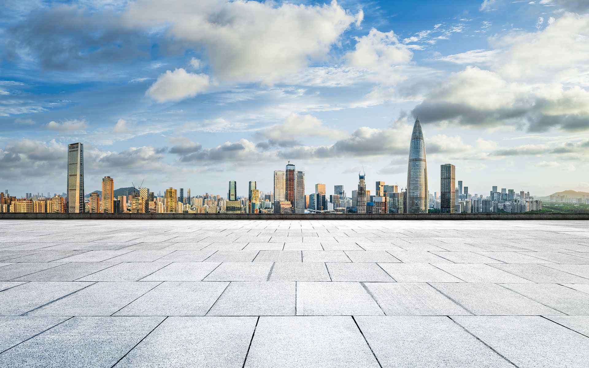 City skyline against a cloudy sky, viewed from a tiled, gray surface.