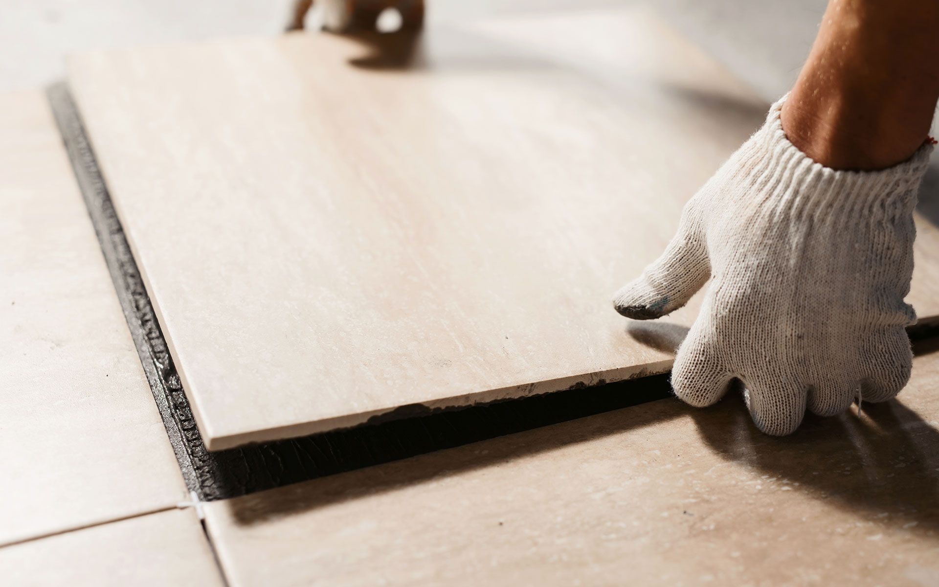 Gloved hand placing a tile onto a bed of adhesive during floor installation.