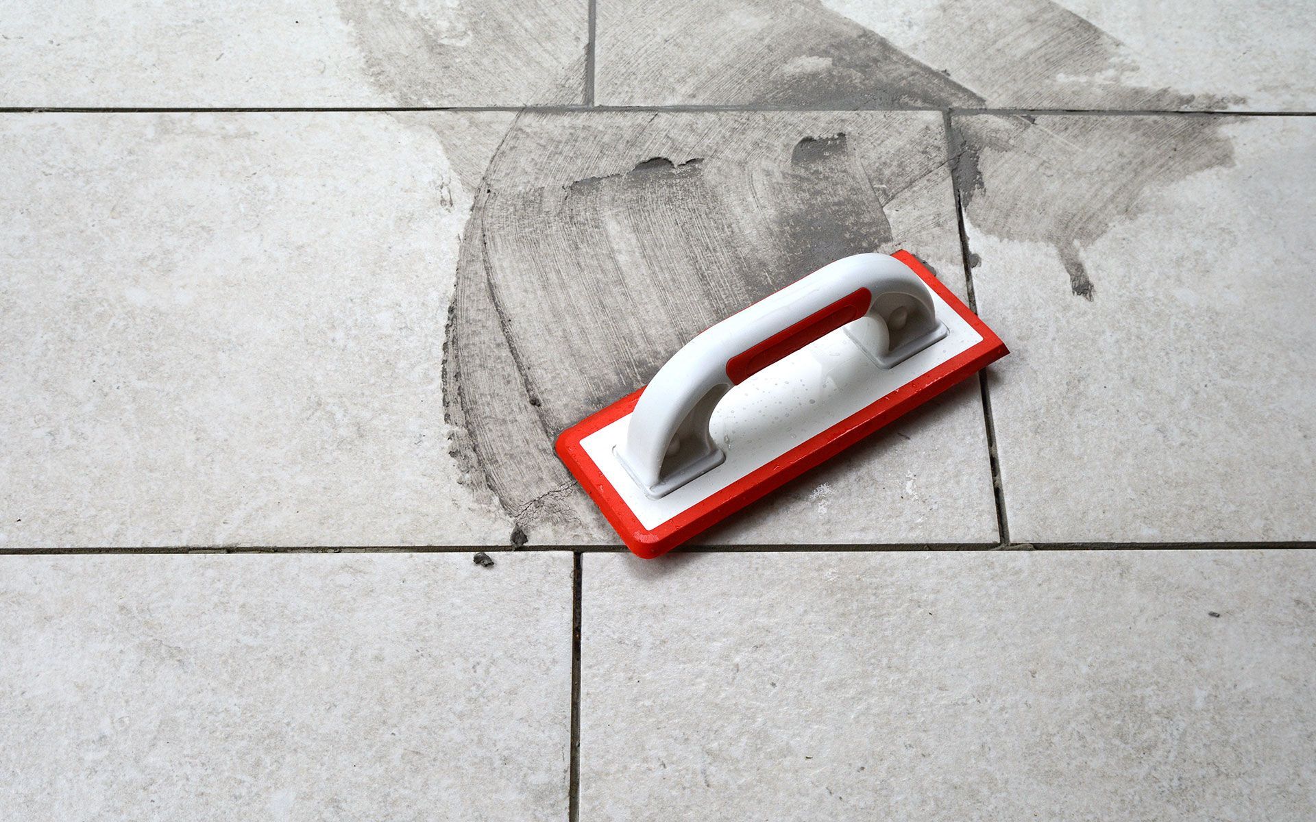 A red and white grout float on light tiles, smearing dark grout.