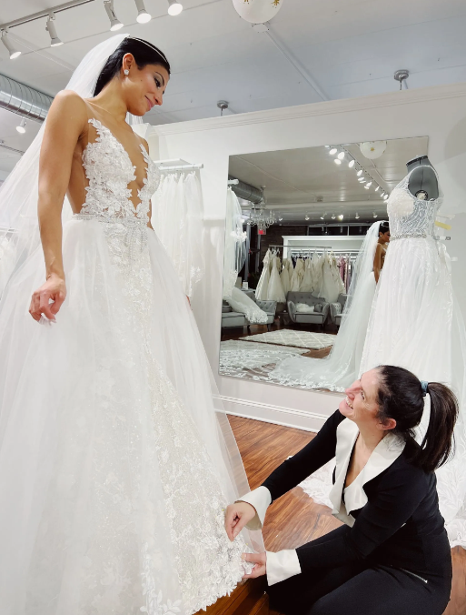 A woman is helping a woman try on a wedding dress