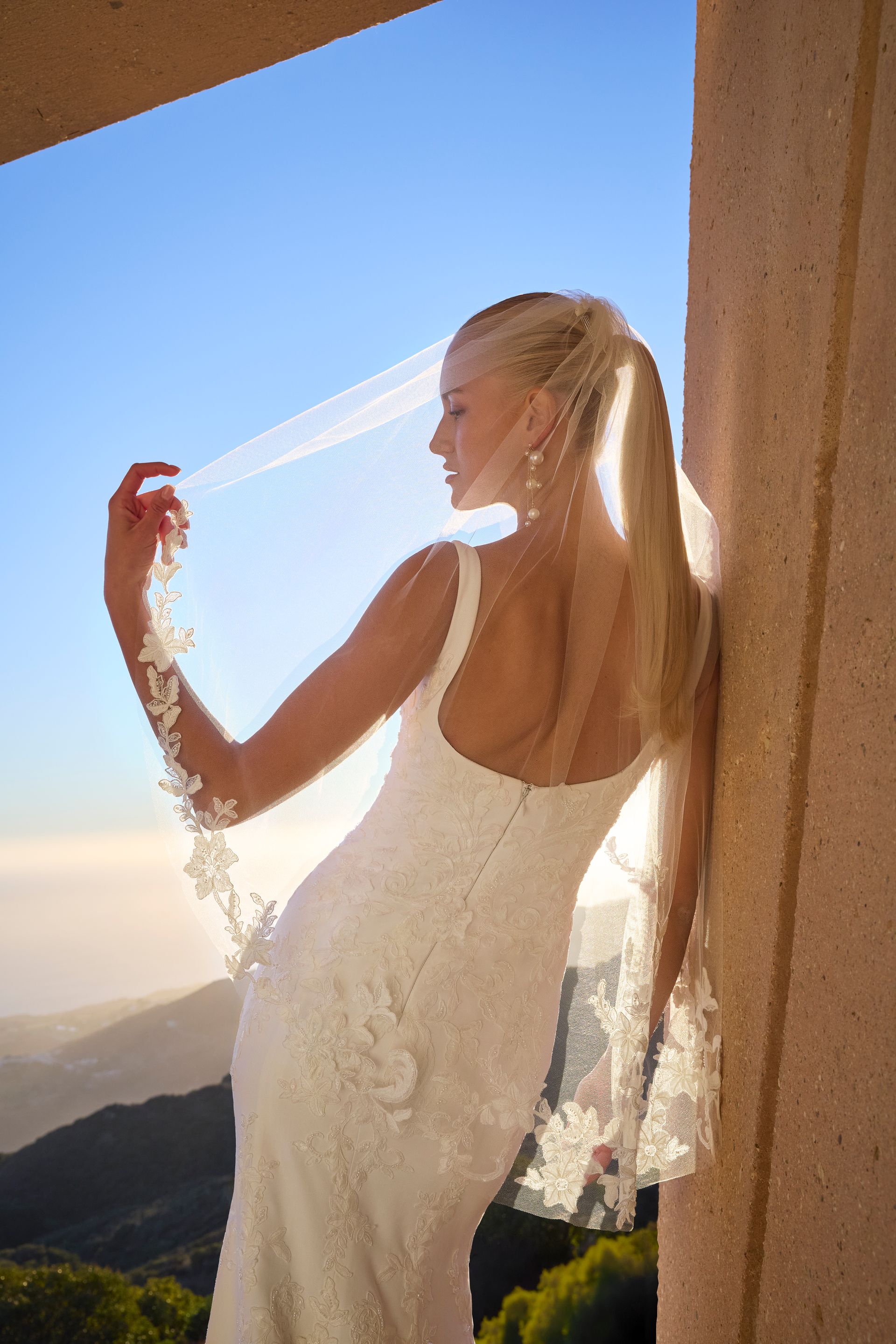 A woman in a wedding dress and veil is leaning against a wall.