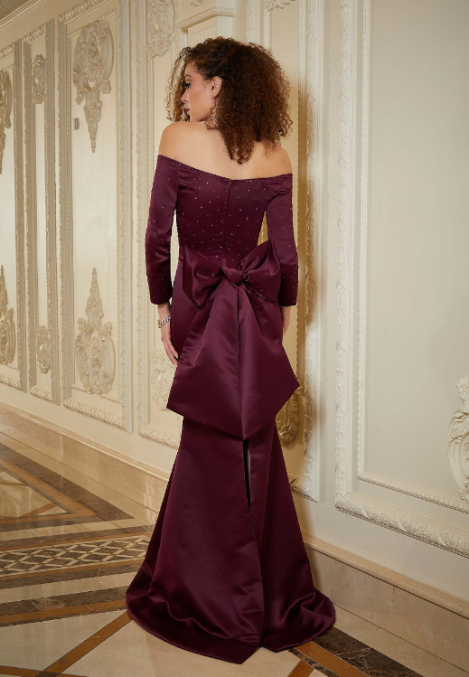 A woman in a purple dress with a bow on the back is standing in a hallway.