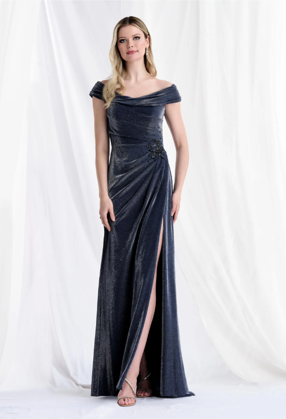 Woman in a navy blue sparkly off-the-shoulder gown, posing in front of a white draped background. The dress has a high slit.
