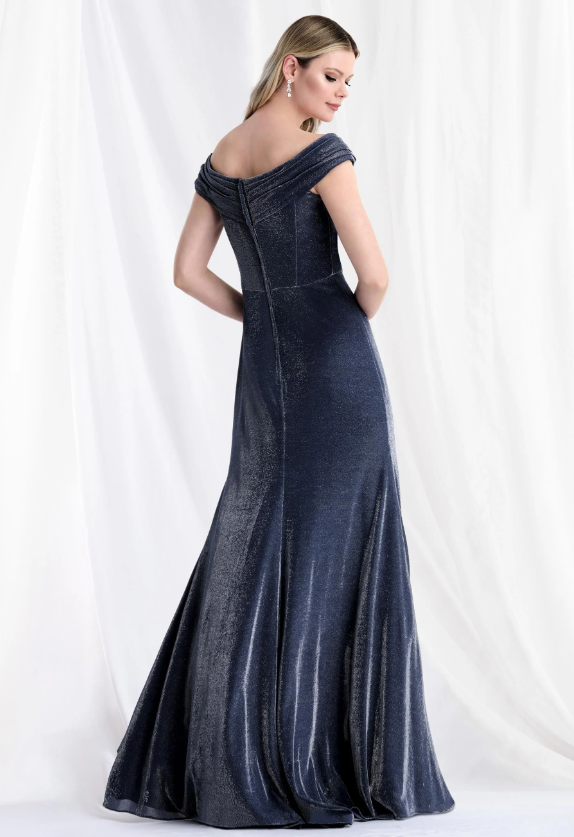 Woman in a navy blue, off-the-shoulder, sparkly evening gown, posing with her back to the camera. She is standing in front of white curtains.