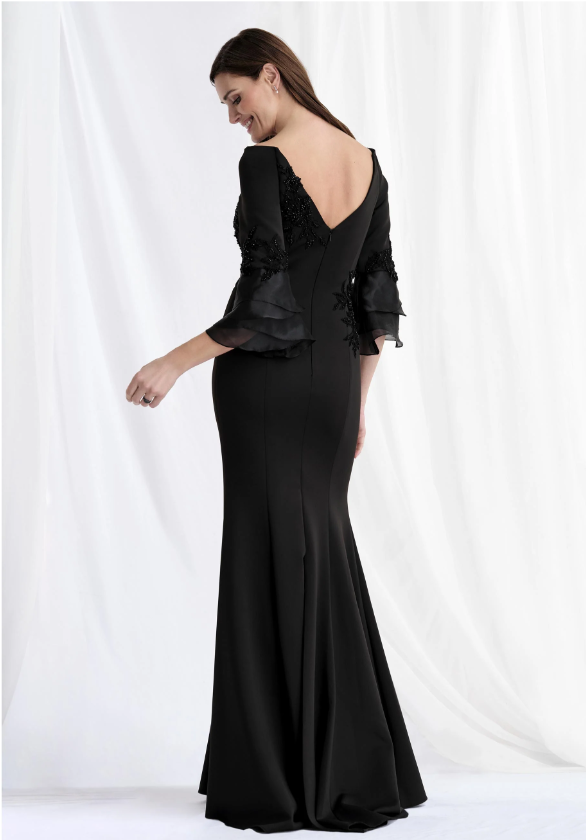 Woman in a long black dress with bell sleeves, turned to the side and smiling in front of a white backdrop.