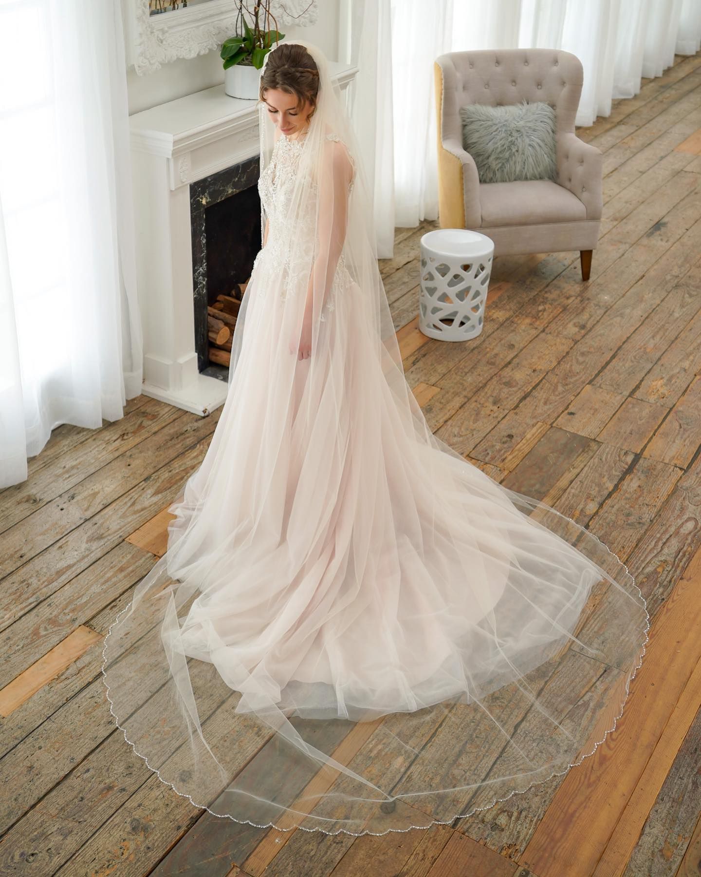 A bride in a wedding dress and veil is standing in front of a fireplace.