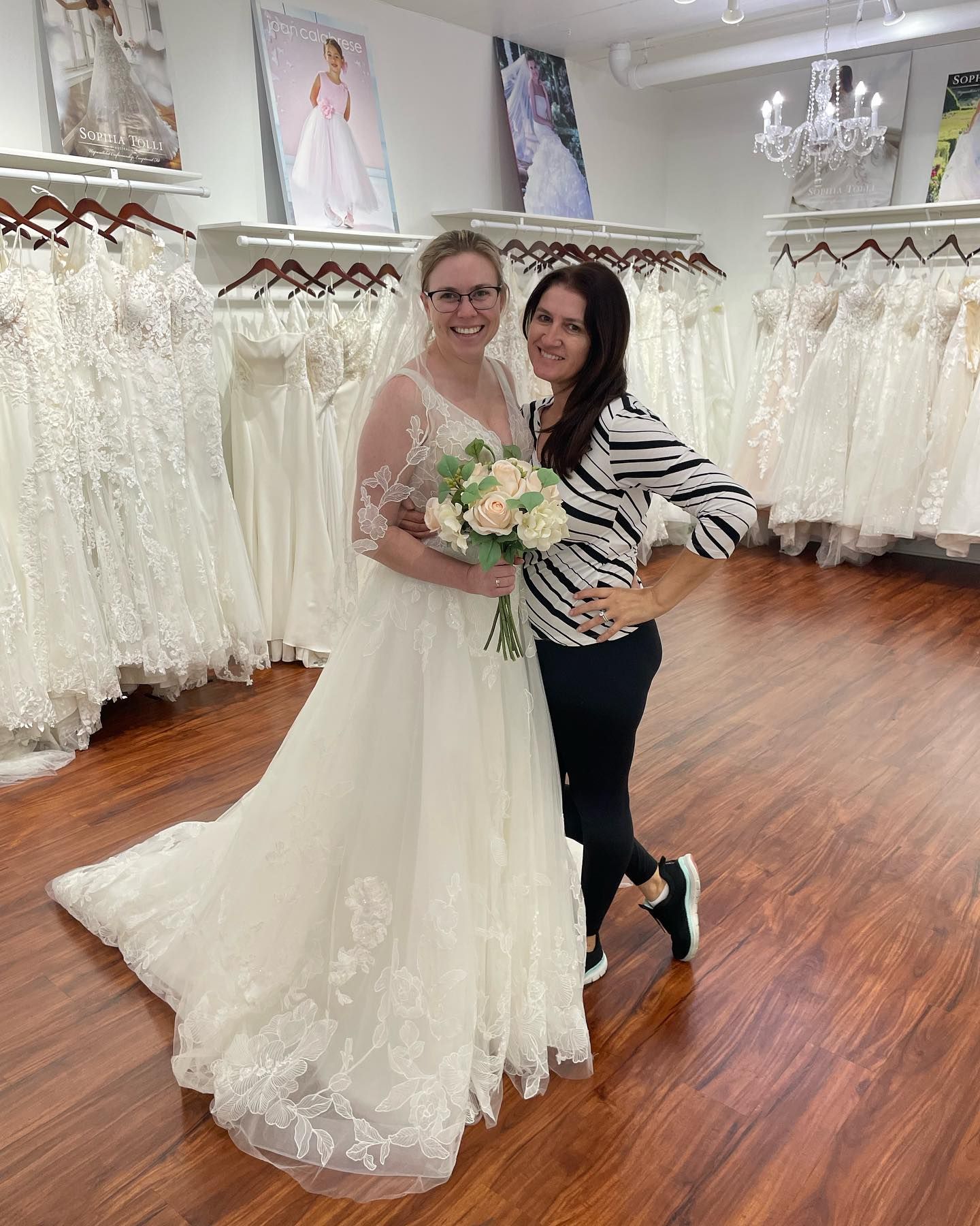 A woman in a wedding dress is standing next to another woman in a bridal shop.