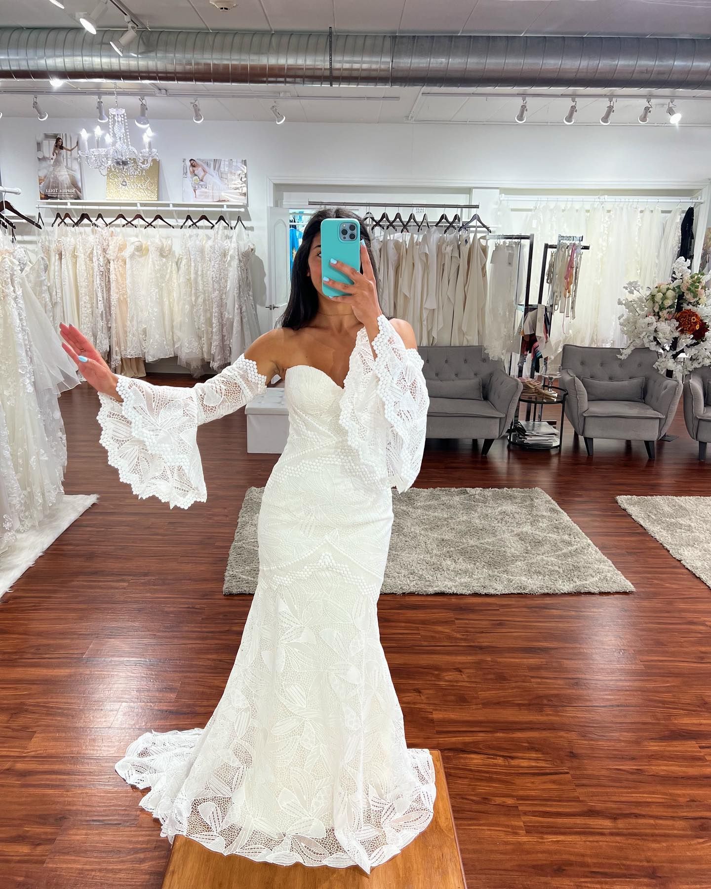 A woman in a wedding dress is taking a selfie in a bridal shop.