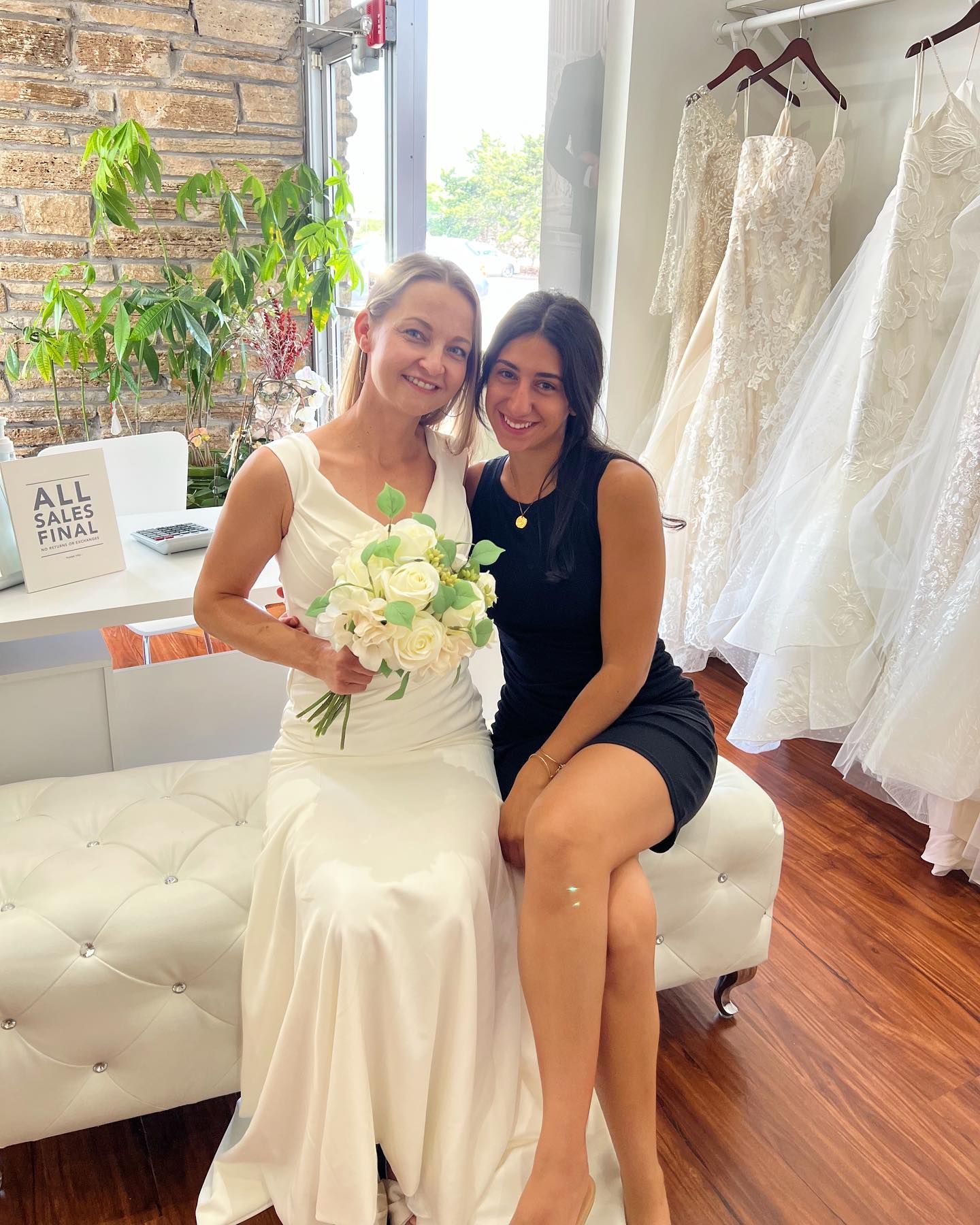 Two women in wedding dresses are posing for a picture in a bridal shop.