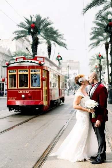 A bride and groom kiss in front of a red trolley
