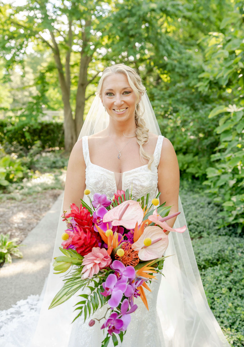 Bride in a white wedding dress with a colorful tropical bouquet, smiling, standing in a garden path. Bride in a white wedding dress with a colorful tropical bouquet, smiling, standing in a garden path.