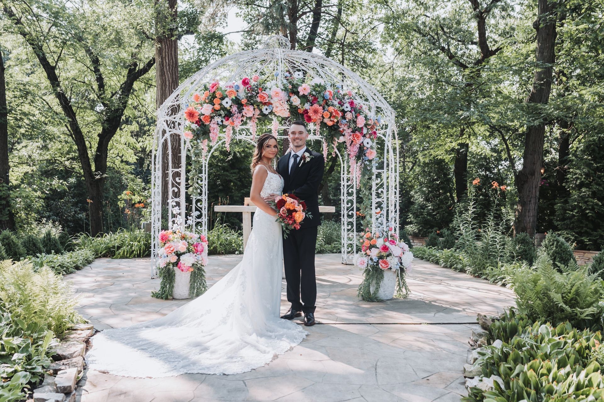 Couple standing under floral arch at outdoor wedding.