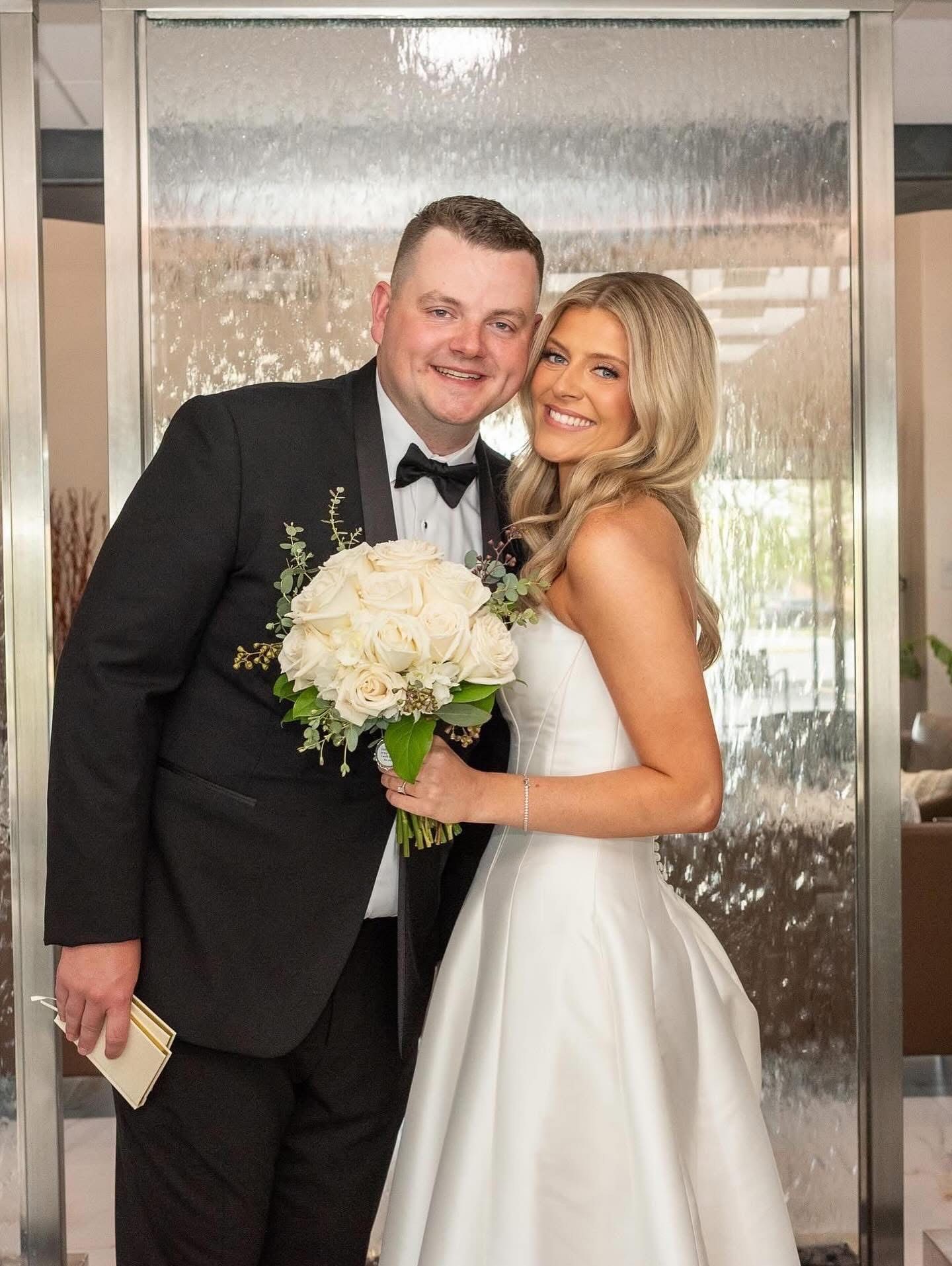 A bride and groom are posing for a picture in front of a waterfall.