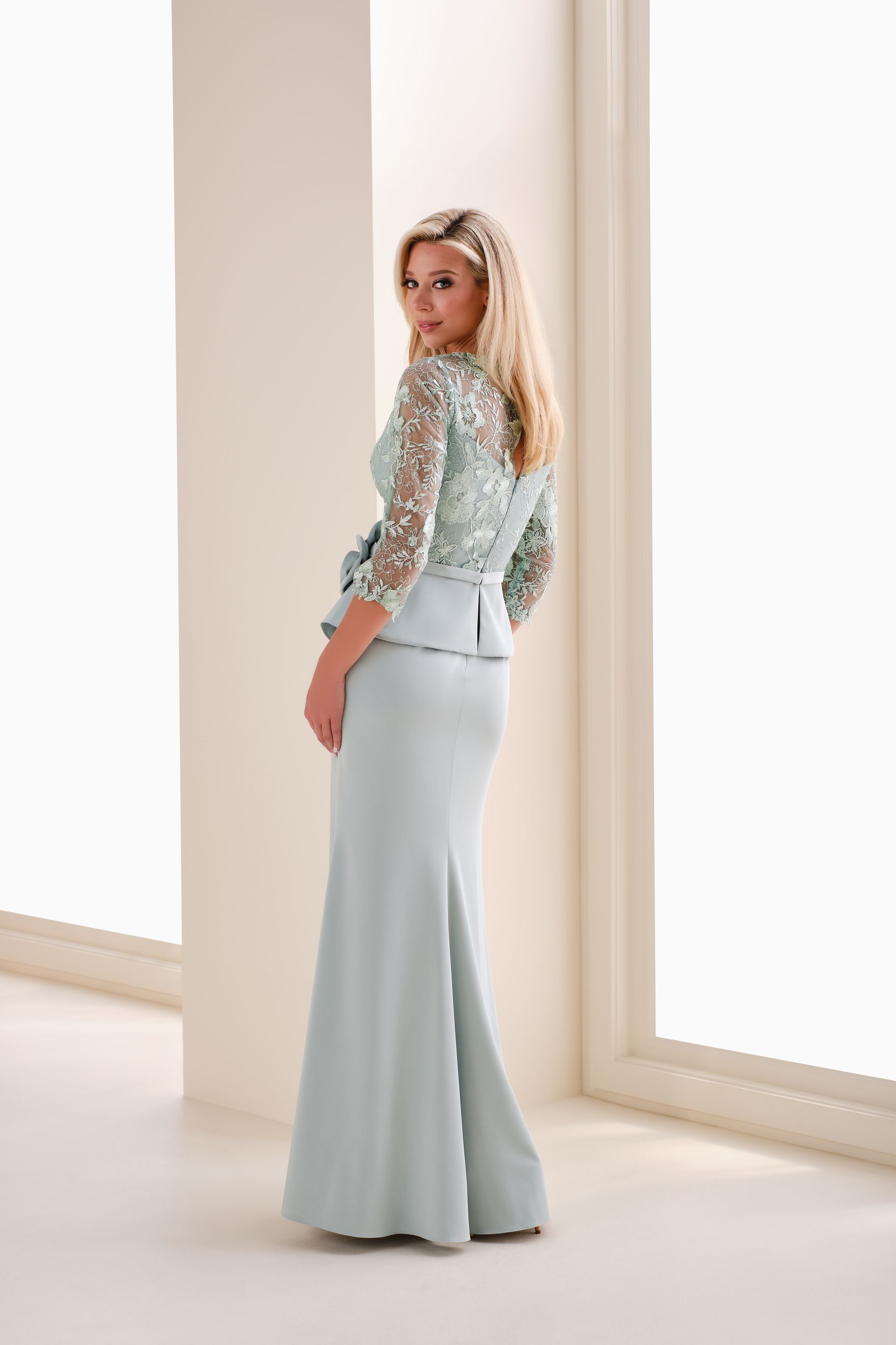 Woman in a light blue formal dress with floral bodice and side slit, standing indoors.