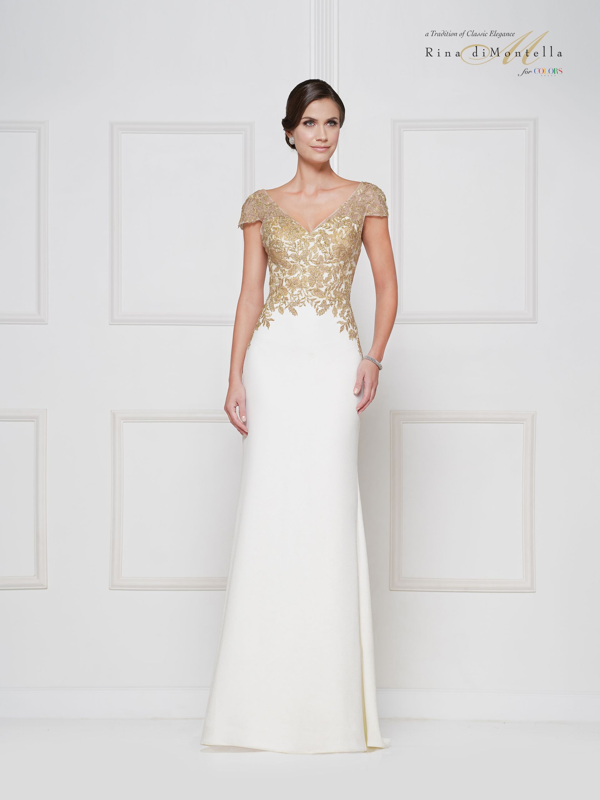 A woman in a white and gold dress is standing in front of a white wall.