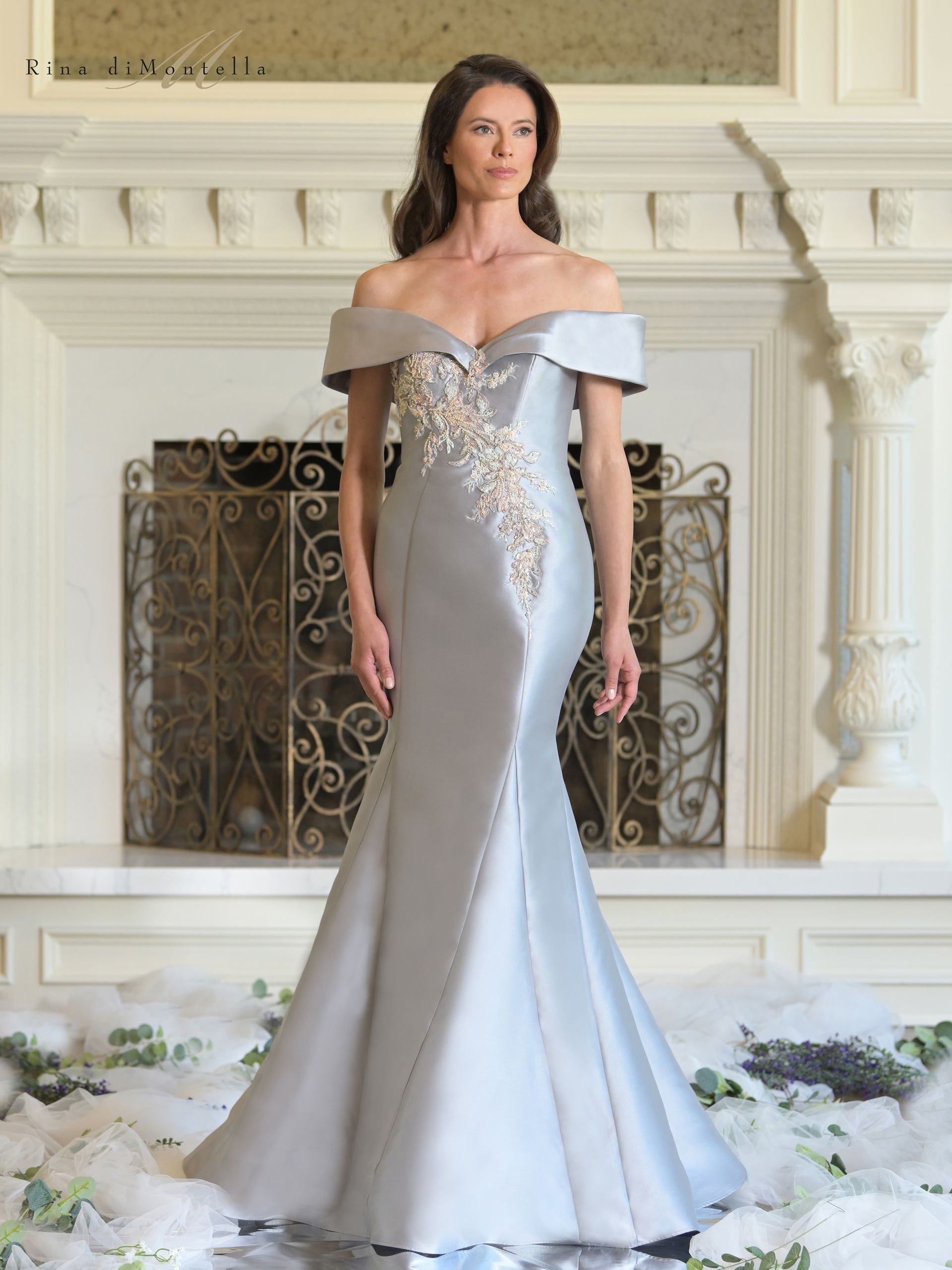 A woman in a long dress is standing in front of a fireplace.