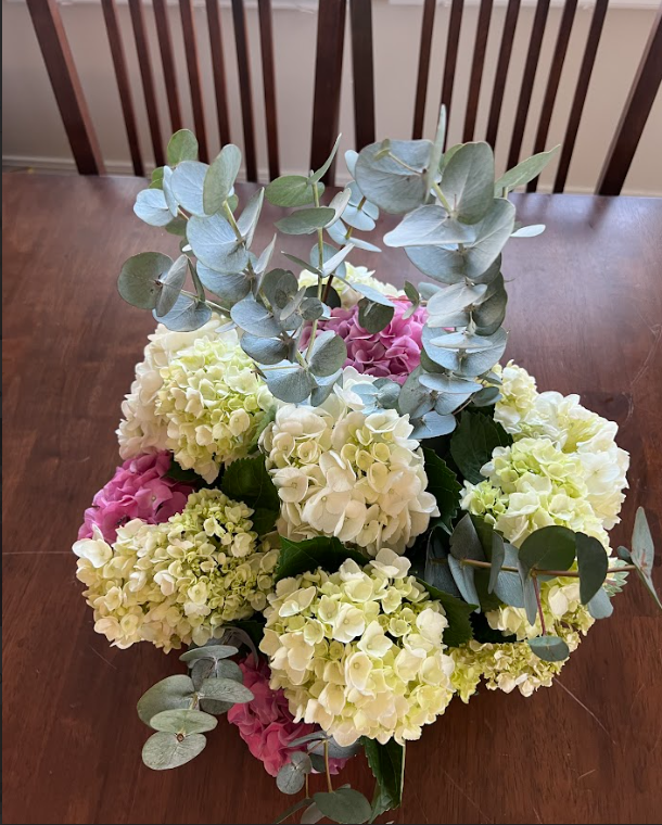 A bouquet of flowers is sitting on a wooden table next to a chair.