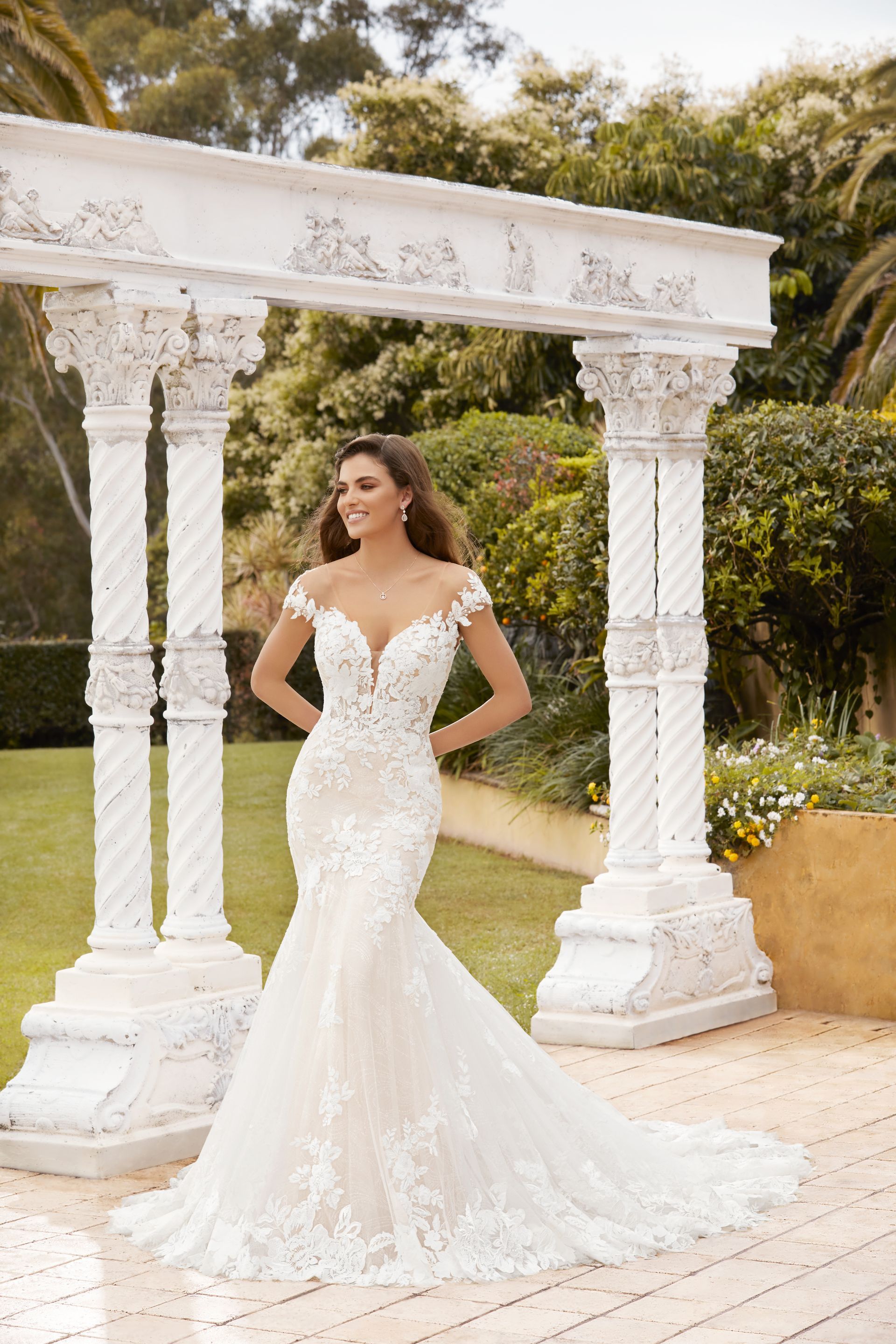 A woman in a wedding dress is standing in front of a white archway.