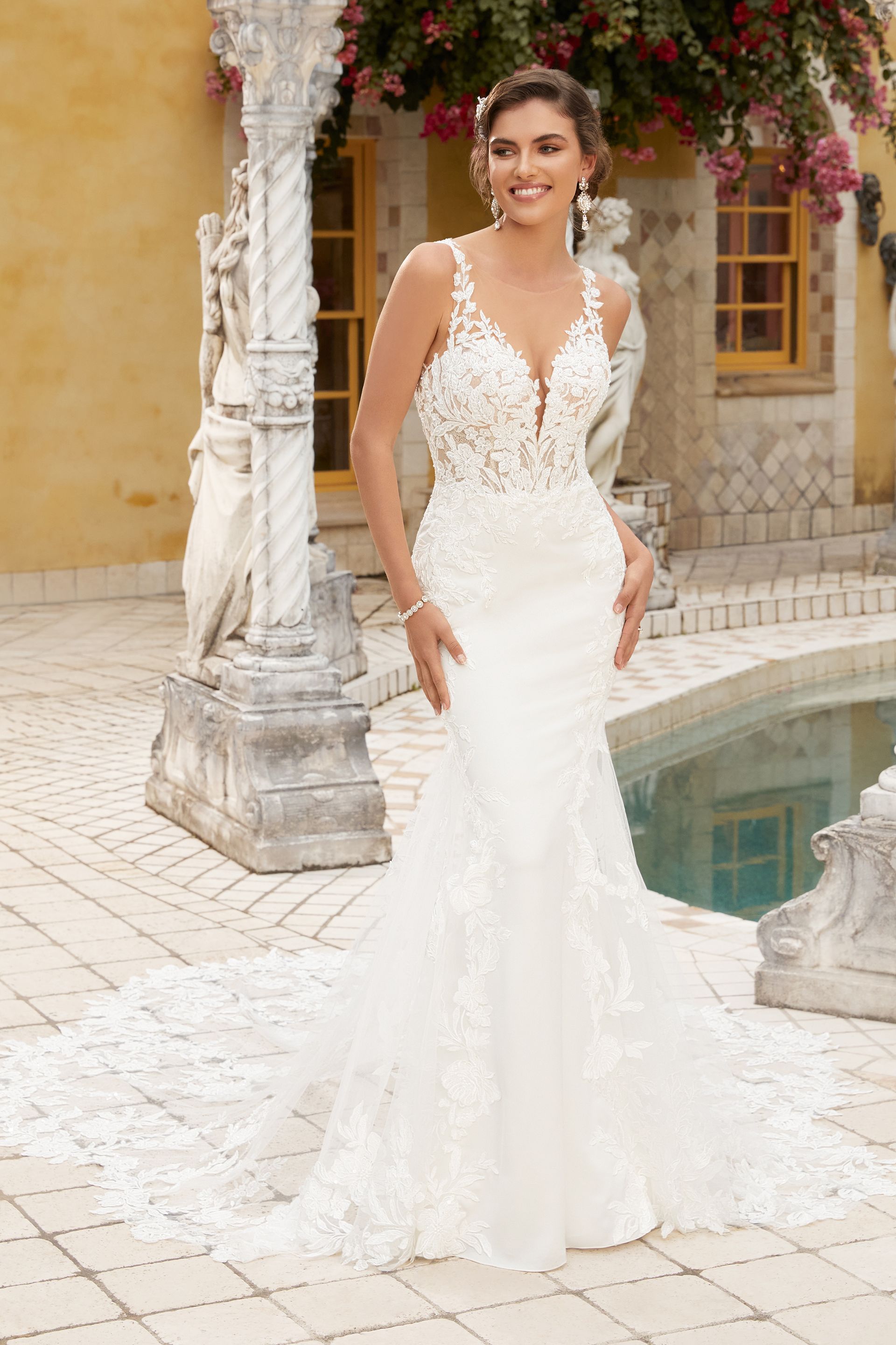 A woman in a white wedding dress is standing next to a pool.