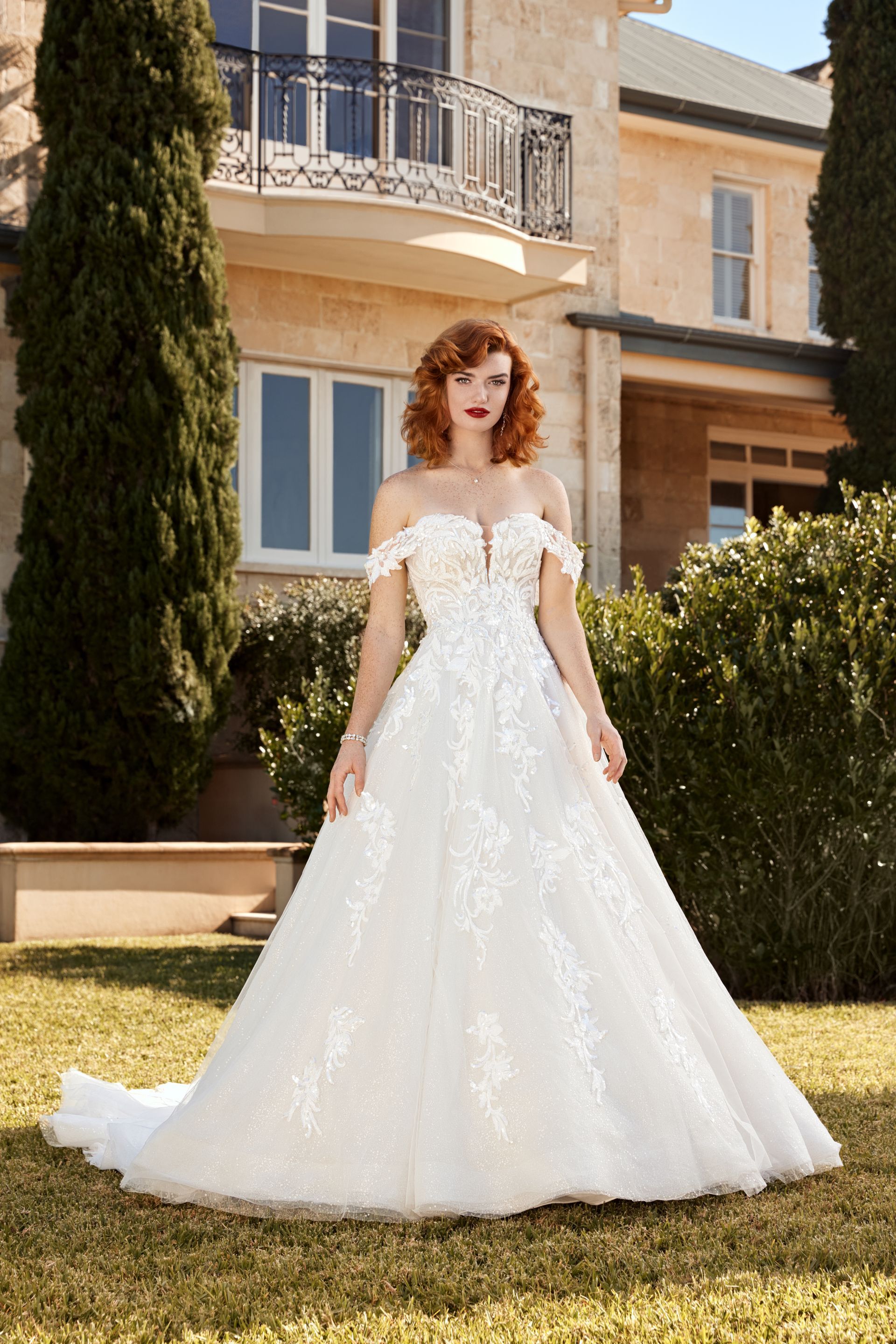 A woman in a white wedding dress is standing in front of a large house.