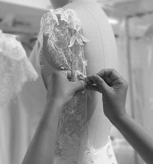 Woman sews on a wedding dress in a well-lit workshop, concentrating intently.
