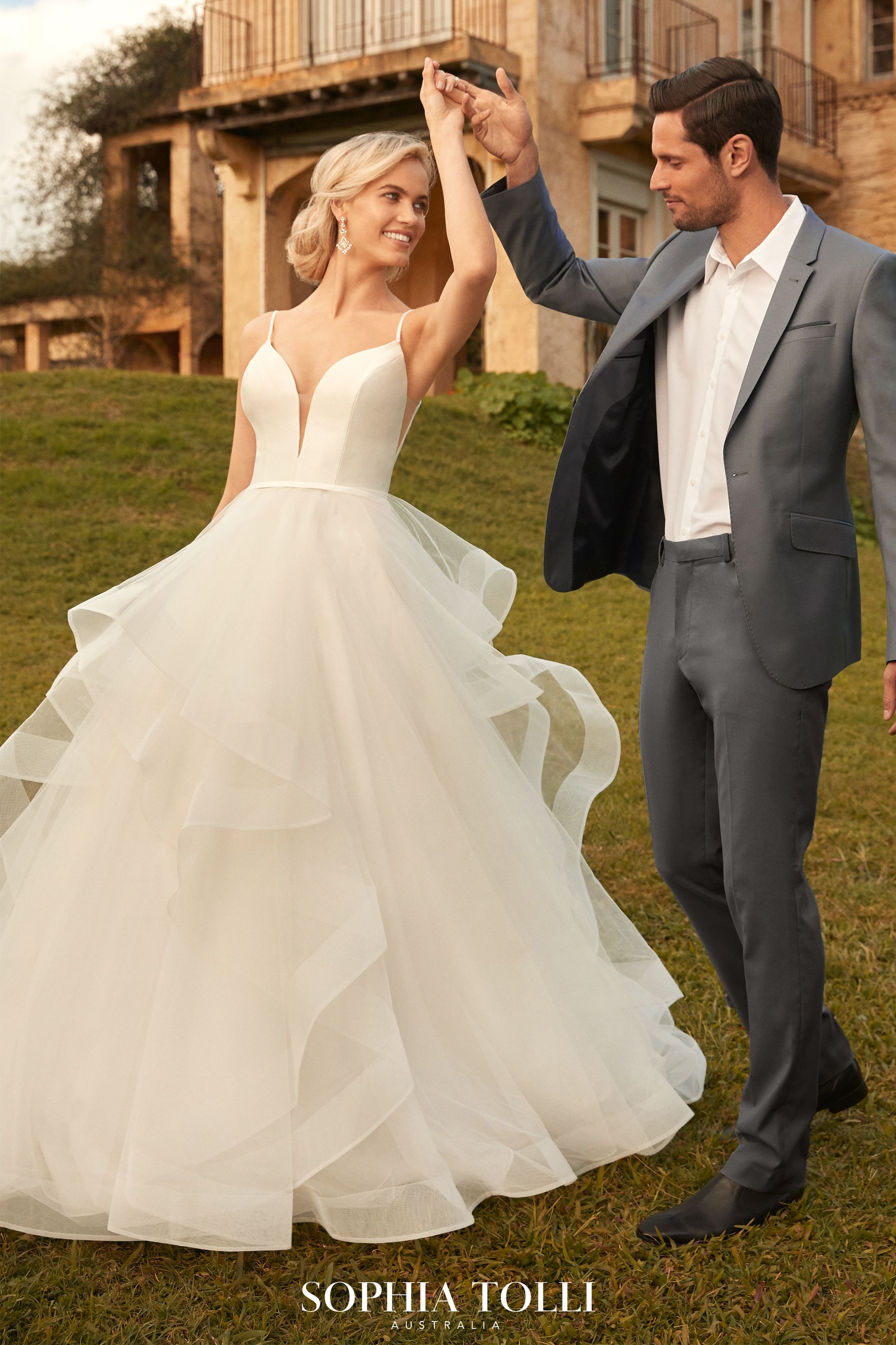 A man in a suit and a woman in a wedding dress are dancing in a field.