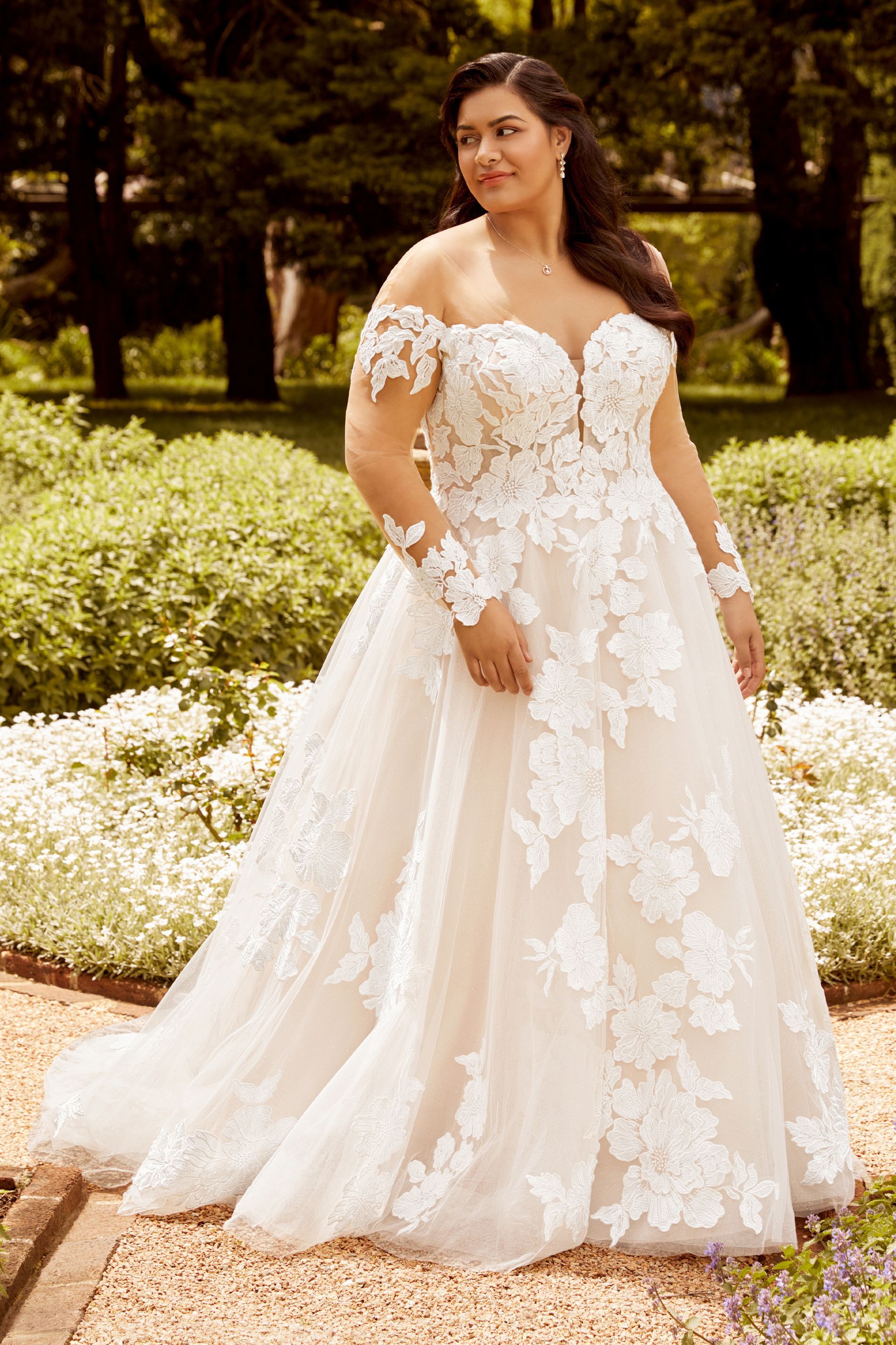 A plus size bride in a white wedding dress is standing in a garden.