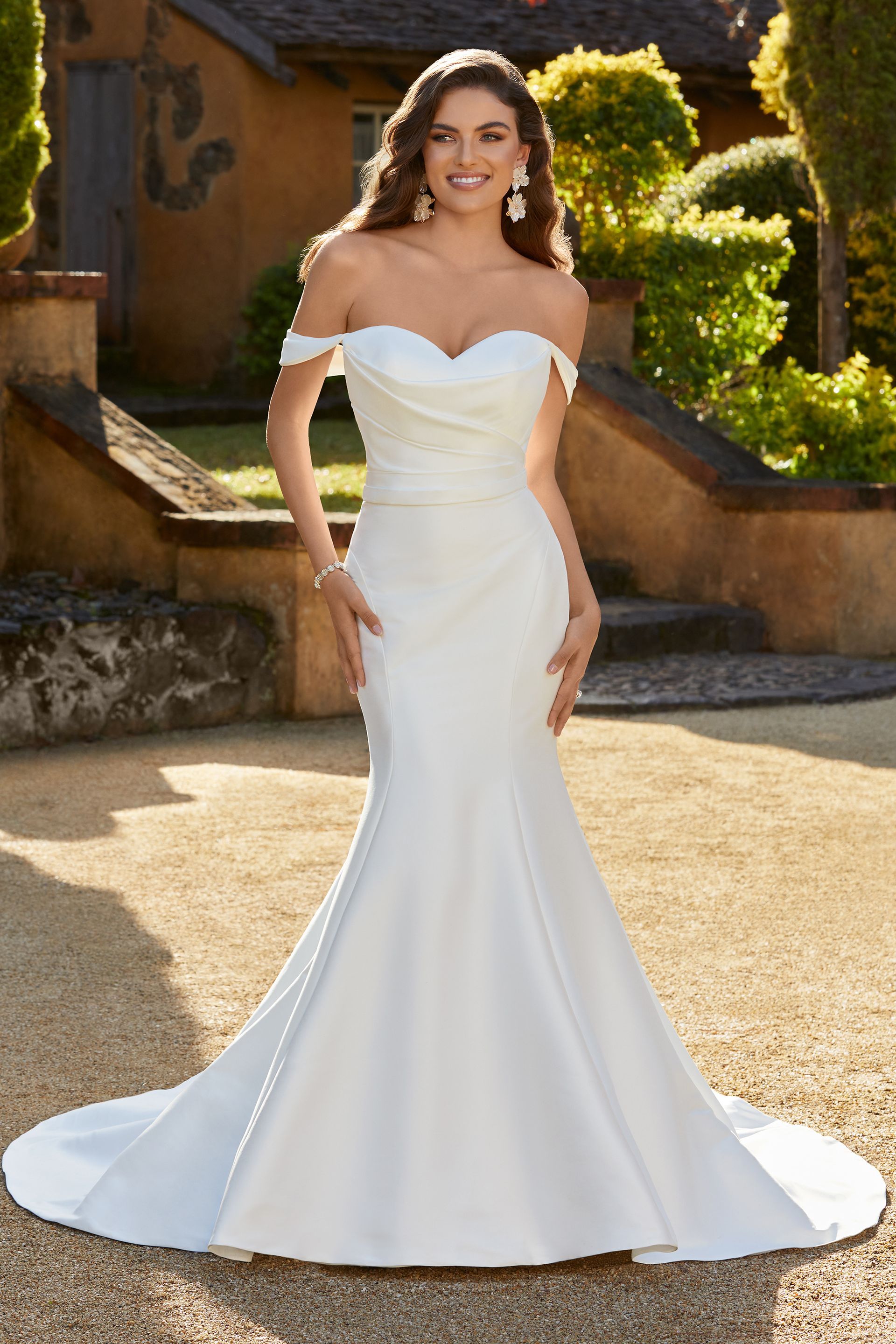 A woman is wearing a white off the shoulder wedding dress.