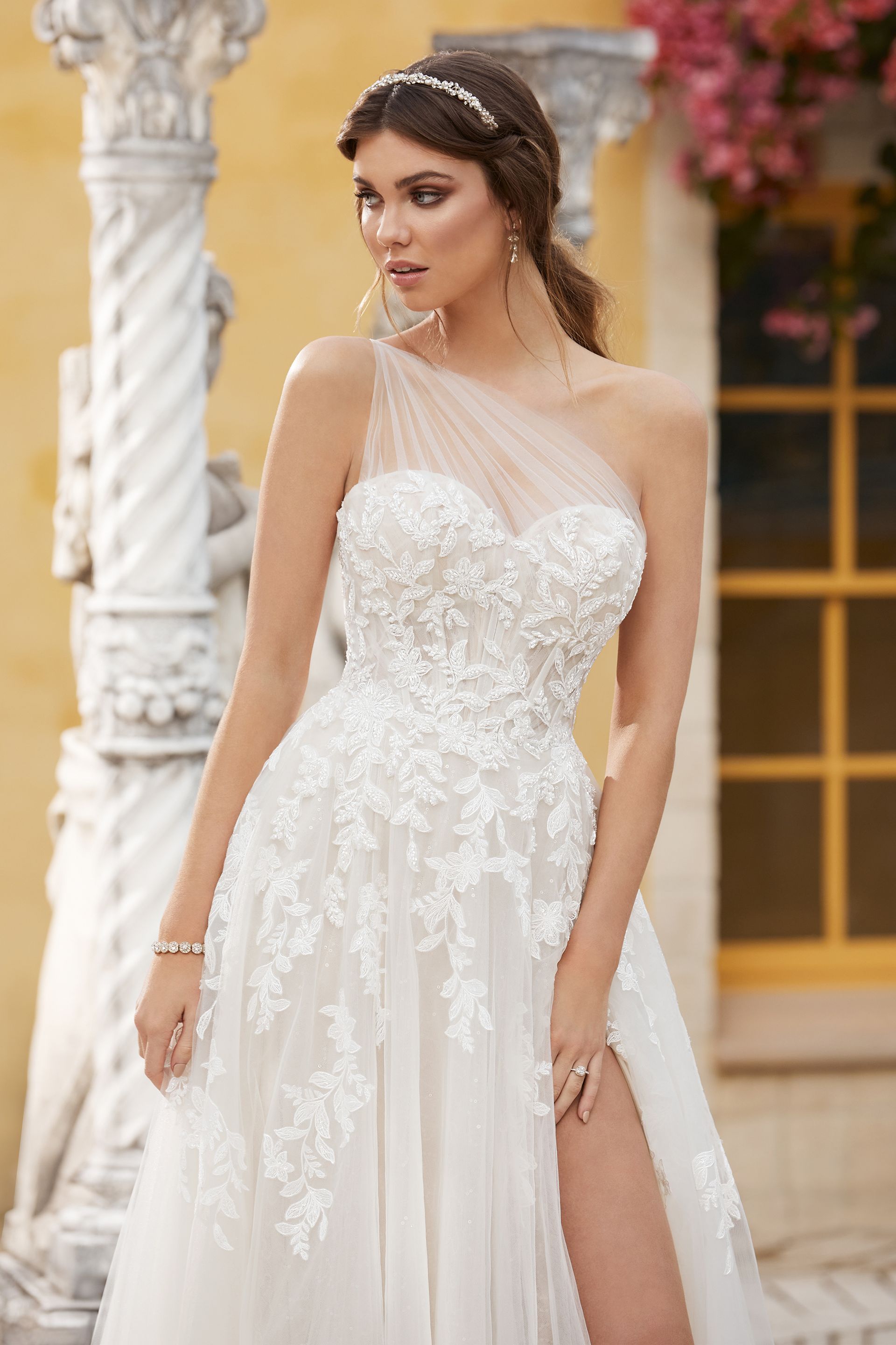 Woman in white wedding dress with one shoulder, slit skirt, and floral embroidery.