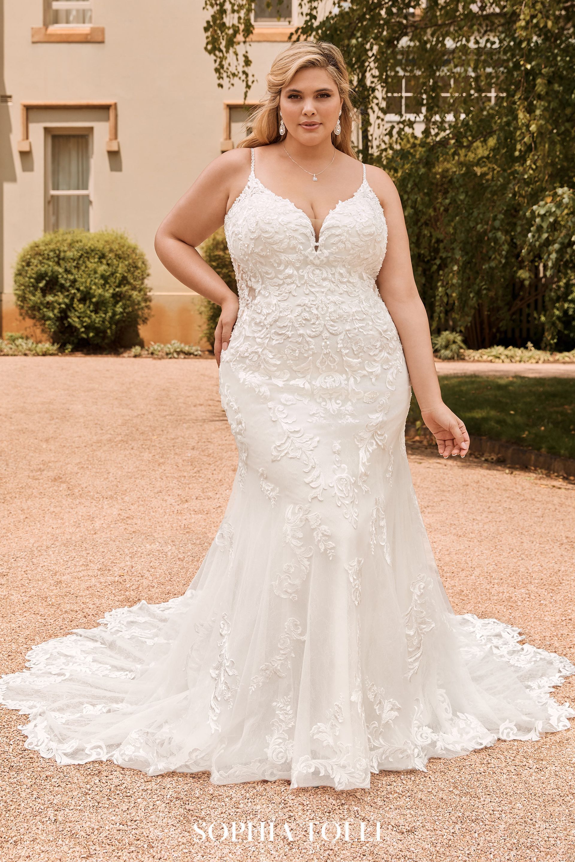 A plus size bride in a white wedding dress is standing in front of a building.