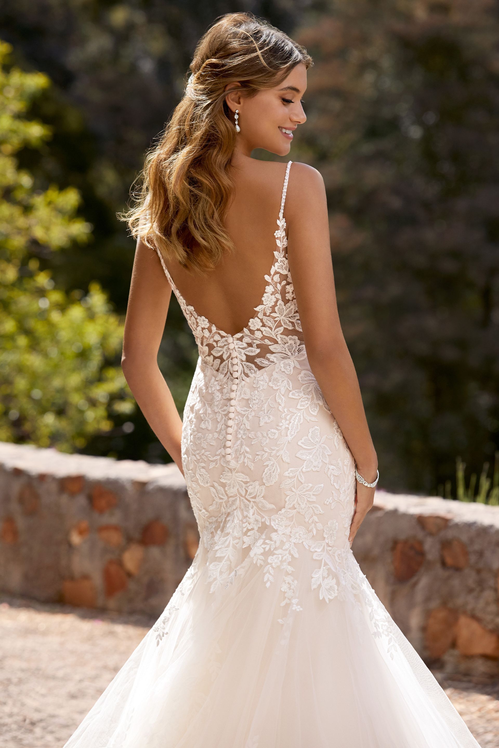 A woman in a white wedding dress is standing next to a stone wall.