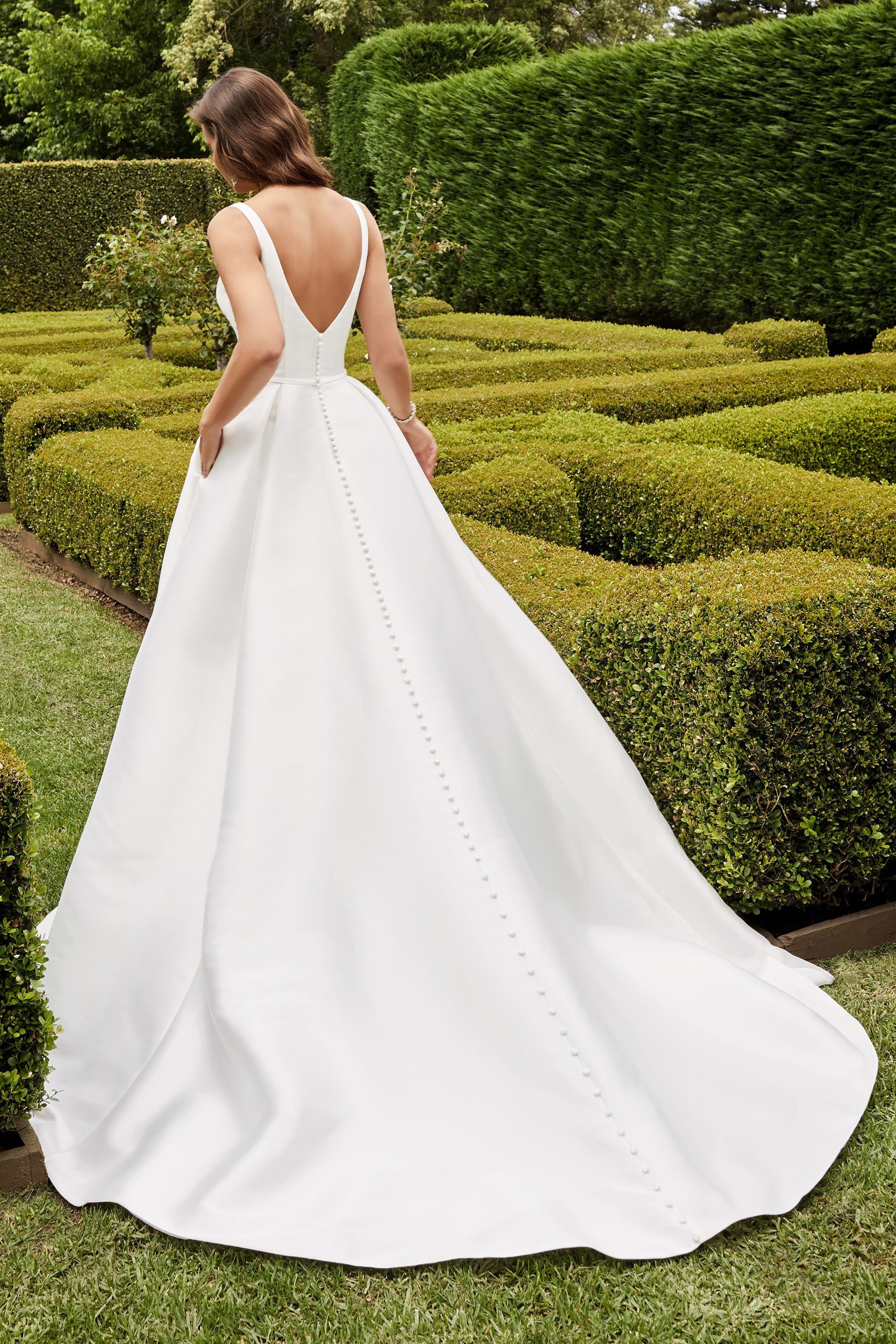 A woman in a white wedding dress is standing in a garden.