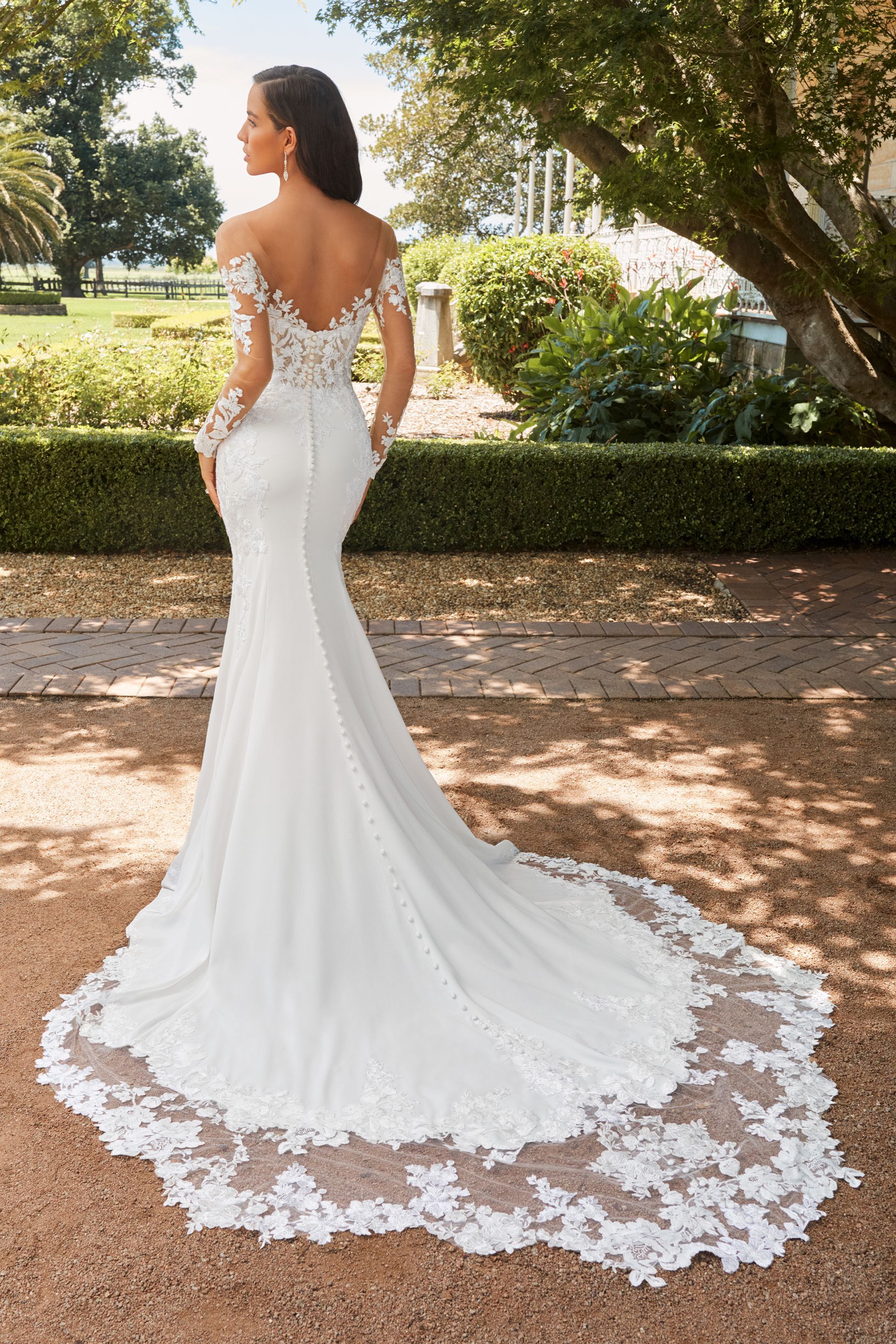 A woman in a Fifi's Bridal white wedding dress is standing in front of a tree.