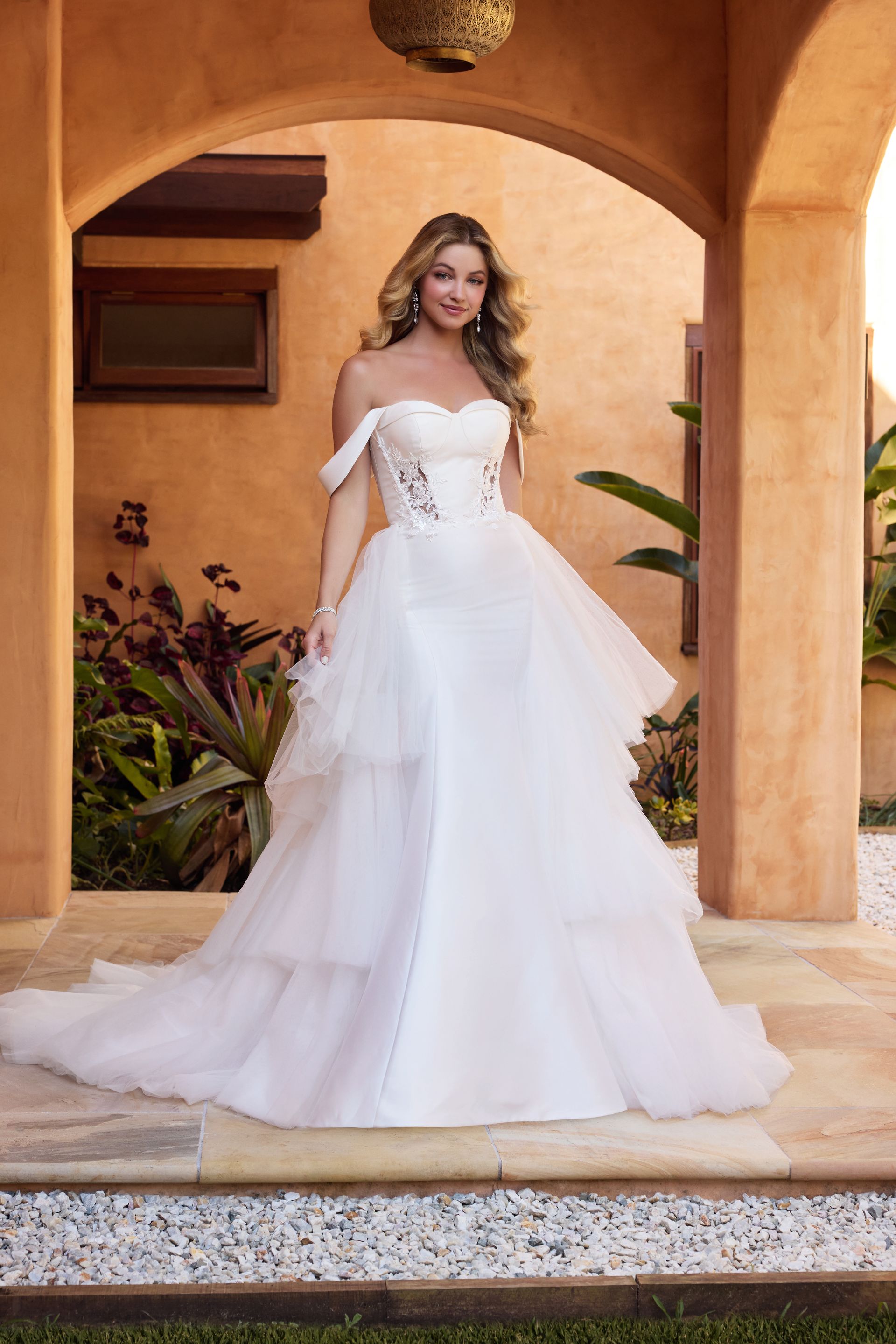 A woman in a white wedding dress is standing in front of a building.