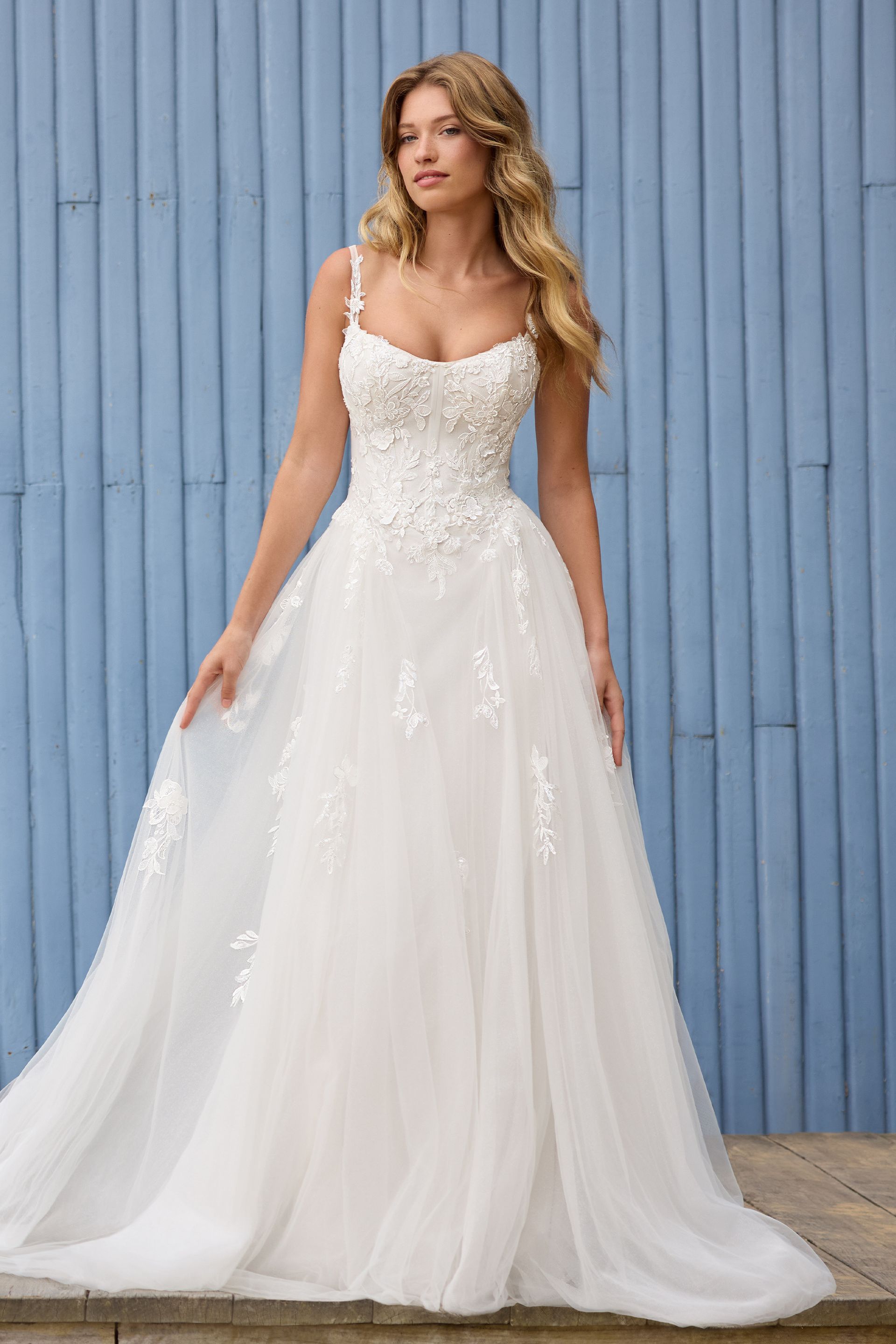 A woman in a white wedding dress is standing in front of a blue wall.