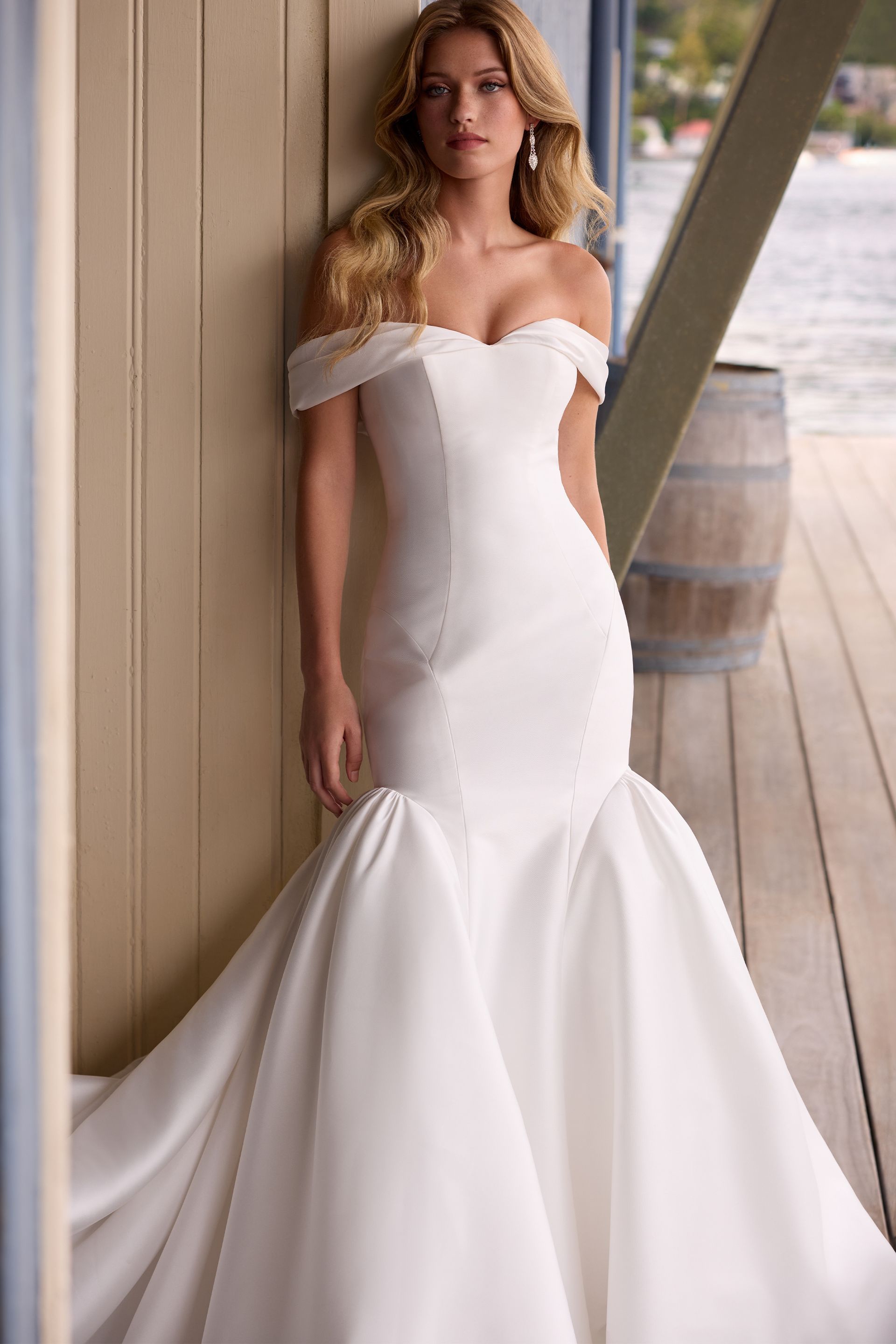 A woman in a white wedding dress is leaning against a wall.