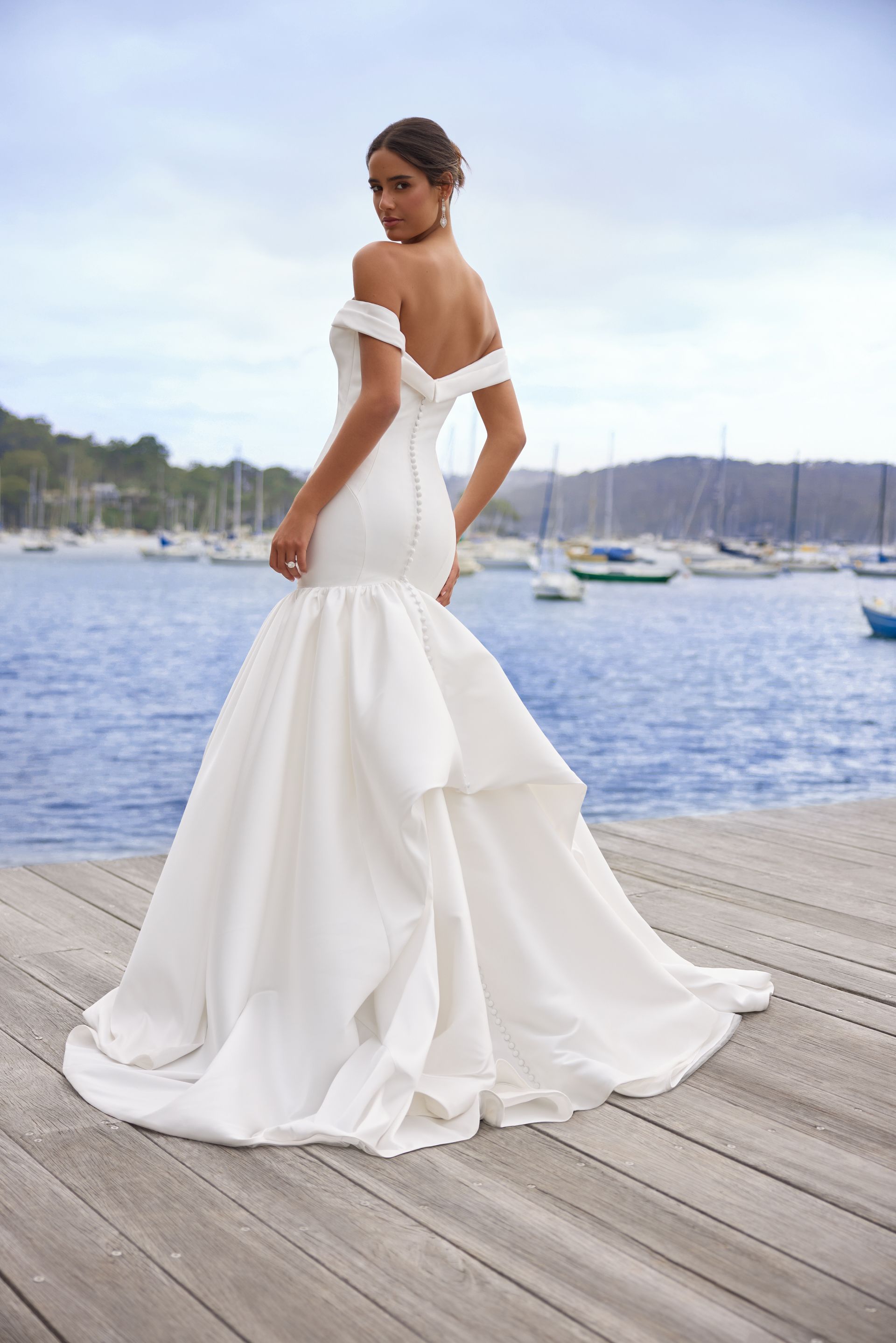 A woman in a white wedding dress is standing on a dock.