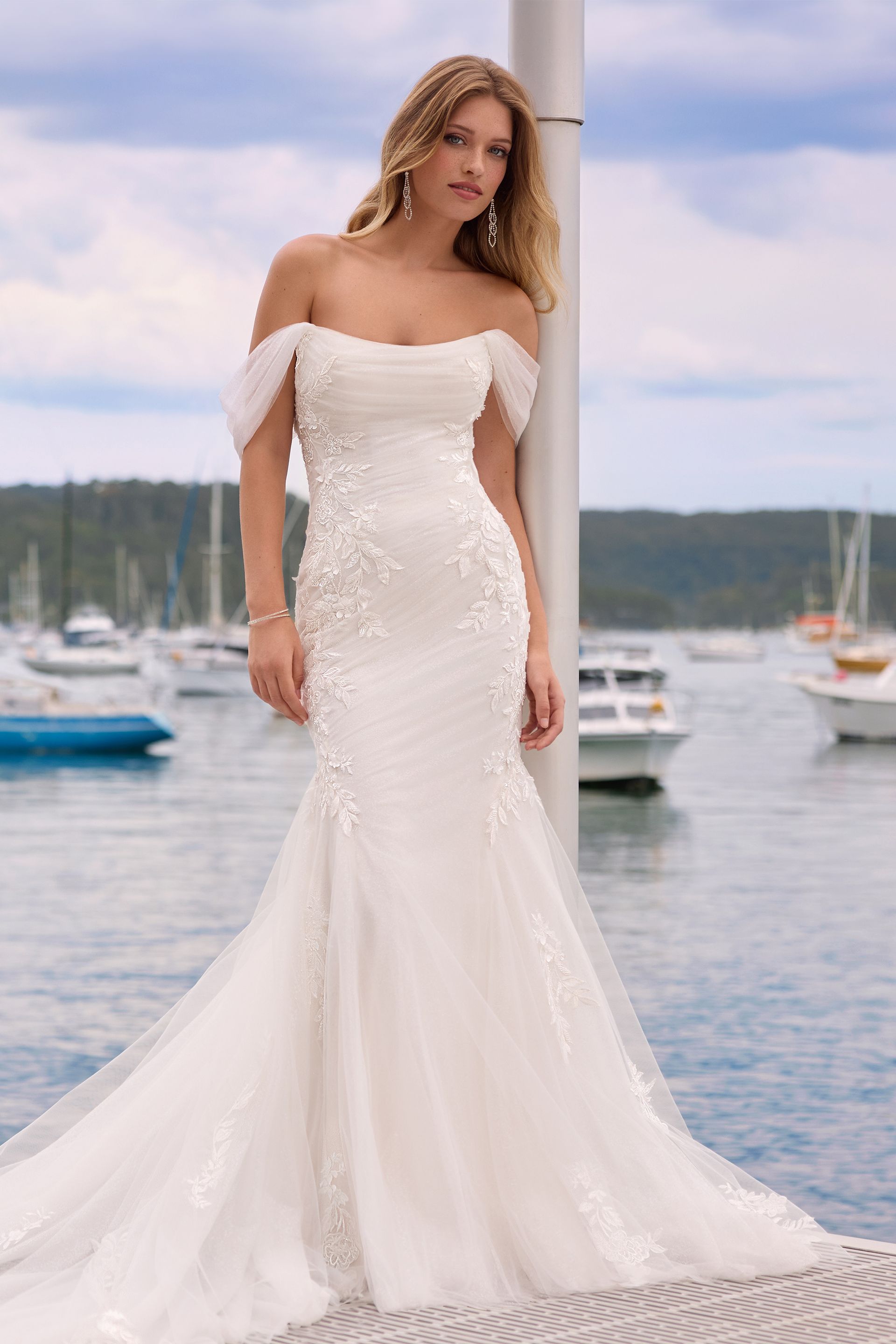 A woman in a white wedding dress is standing next to a pole in front of a body of water. A woman in a white wedding dress is standing next to a pole in front of a body of water.