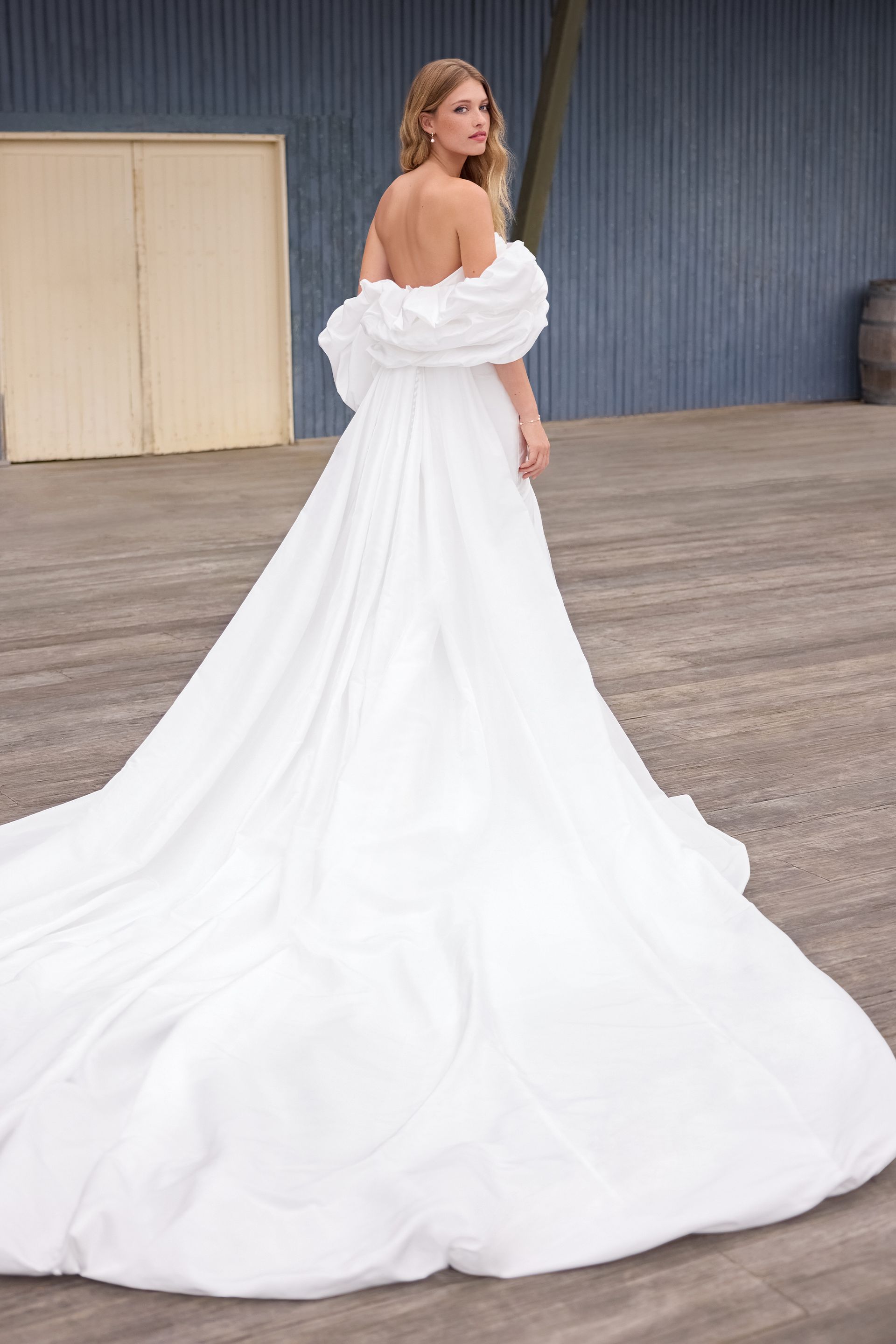 A woman in a white wedding dress is standing on a wooden deck.
