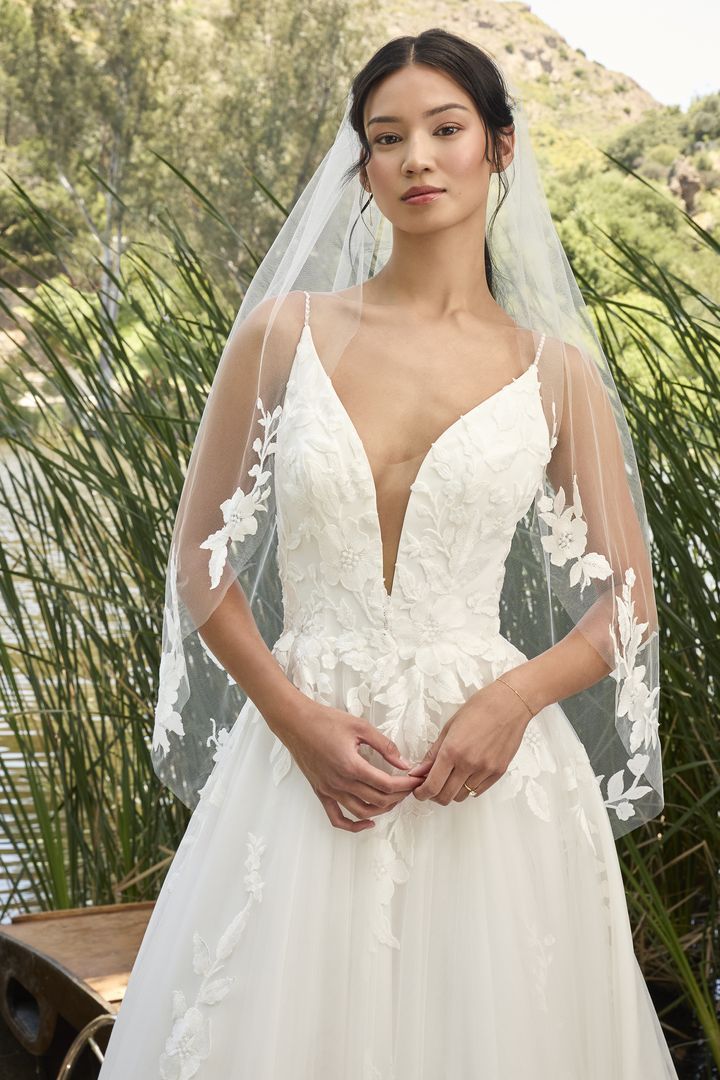 Woman in a white wedding dress with a deep V-neck, wearing a veil, posing outdoors.