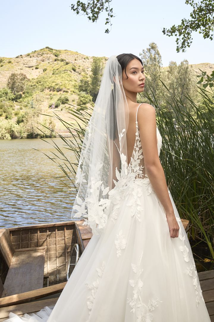 Woman in a white wedding dress with a veil, posing near a lake. She looks over her shoulder.