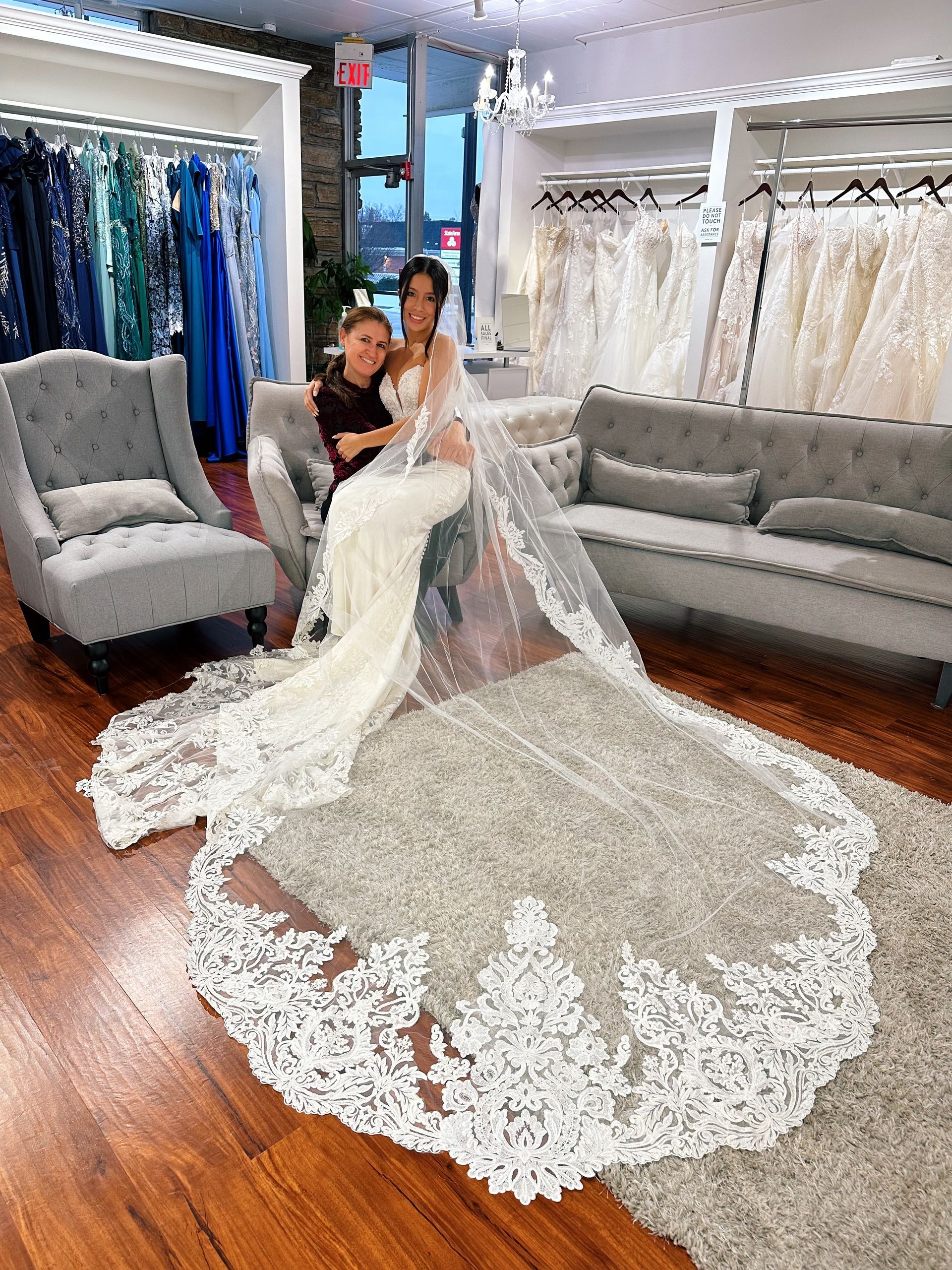 Bride with long veil poses with a woman in a wedding dress shop.