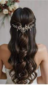 Woman with dark wavy hair styled half up with a jeweled hairpiece; she's wearing a white strapless dress.